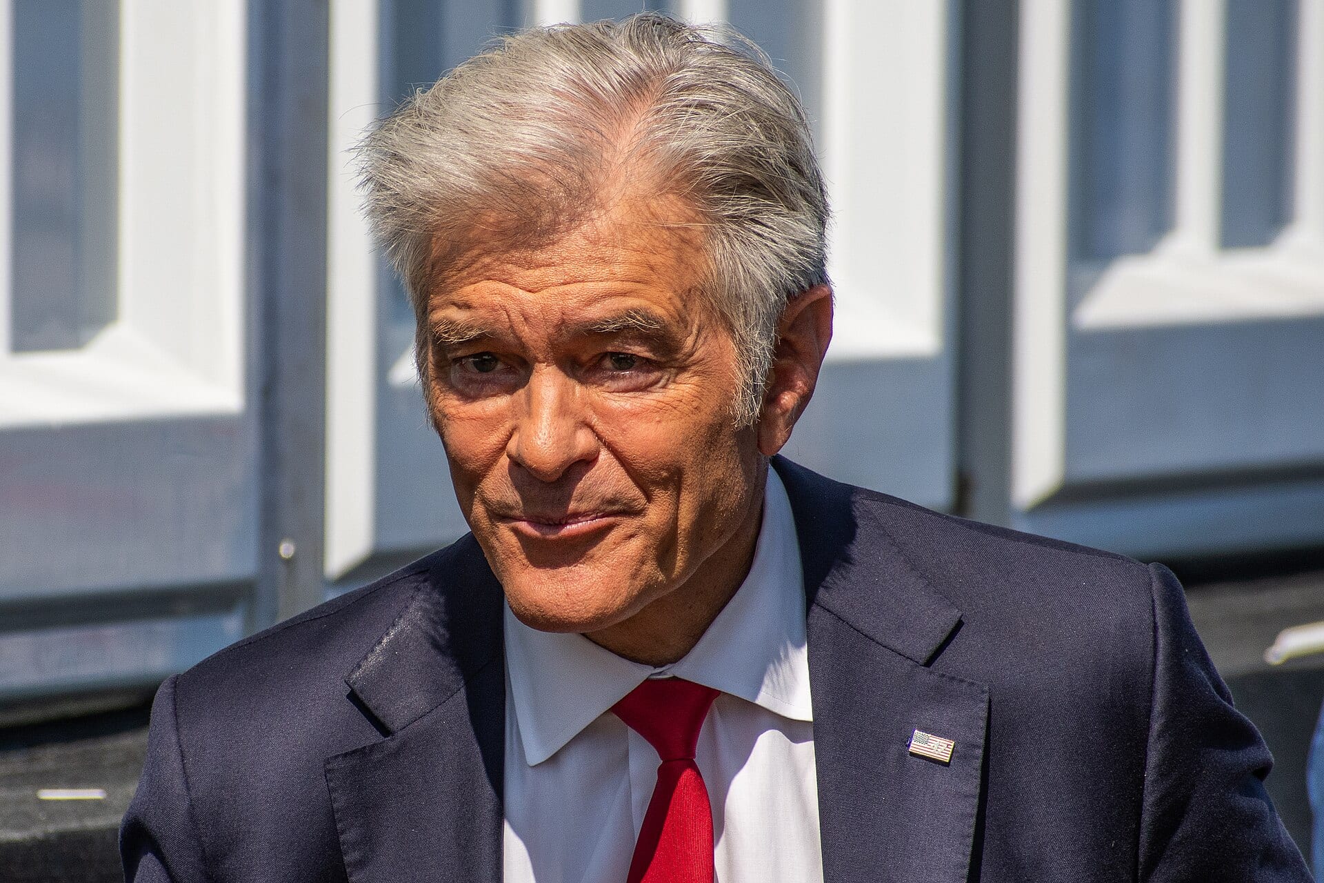 Mehmet Oz in a navy suit and red tie, photographed outdoors