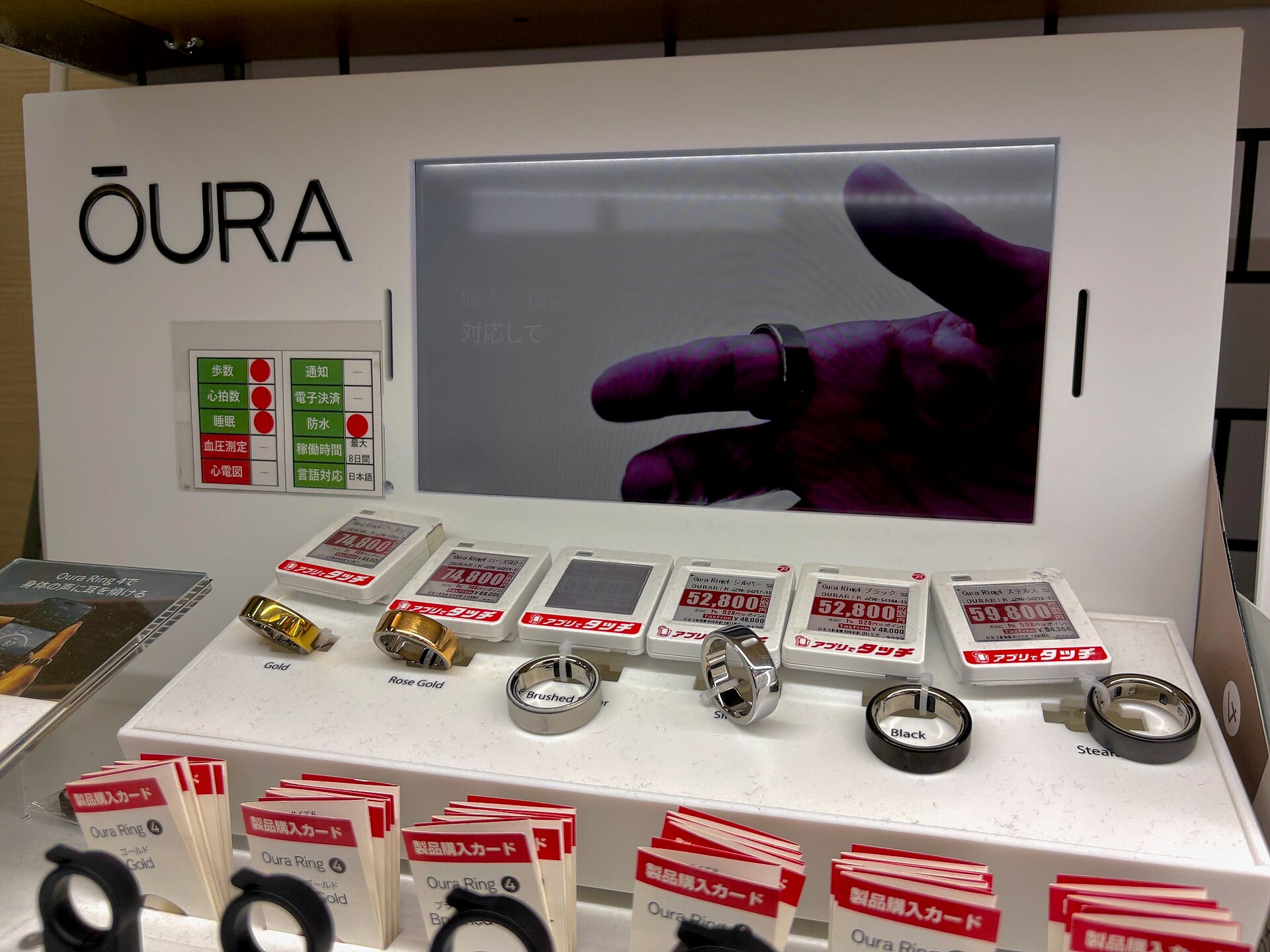 Oura Ring 4 models on display at a Japanese retail counter, with the Oura logo on the wall behind them.