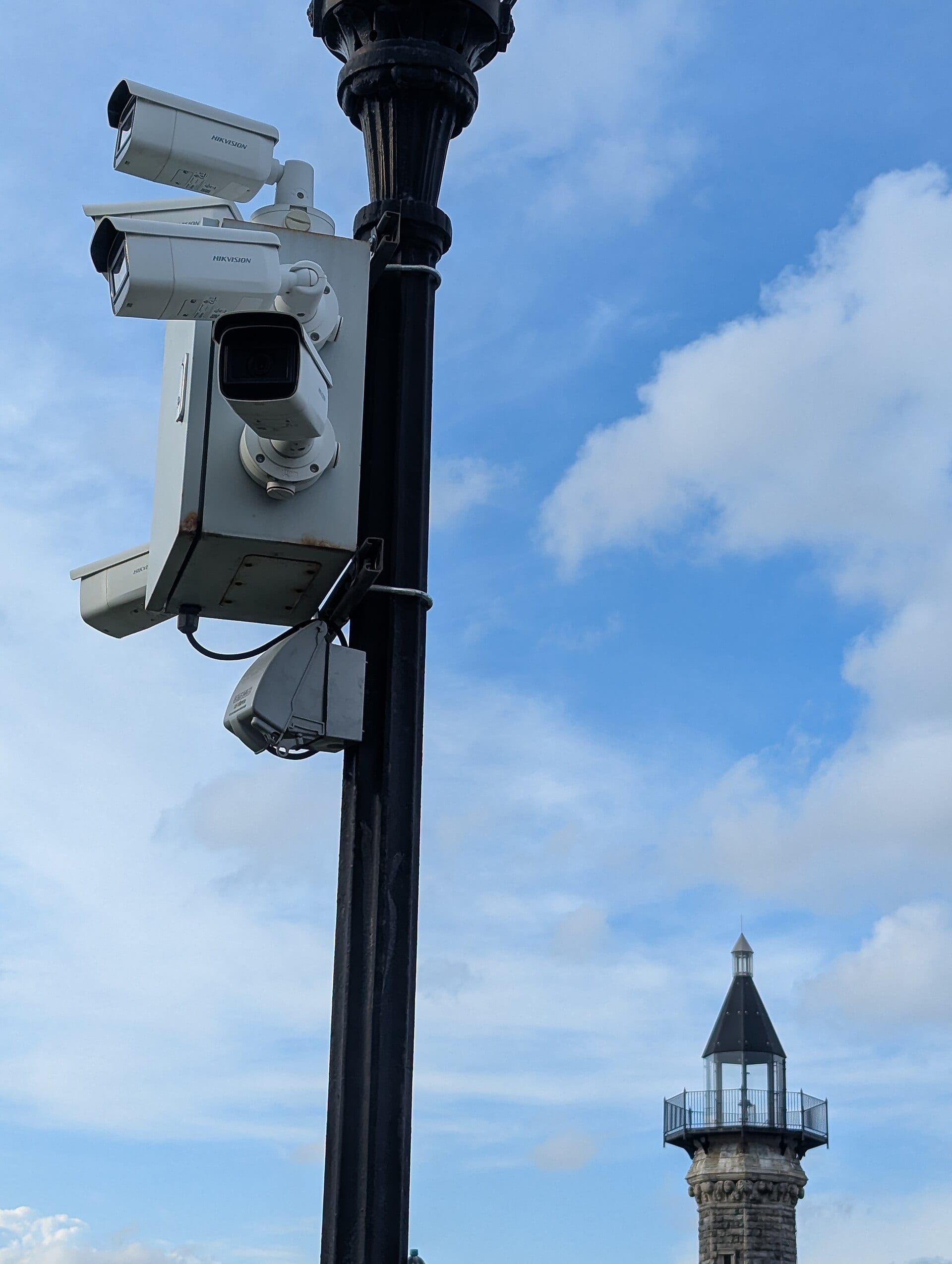 Multiple Hikvision surveillance cameras mounted on a lamppost above Roosevelt Island, New York City