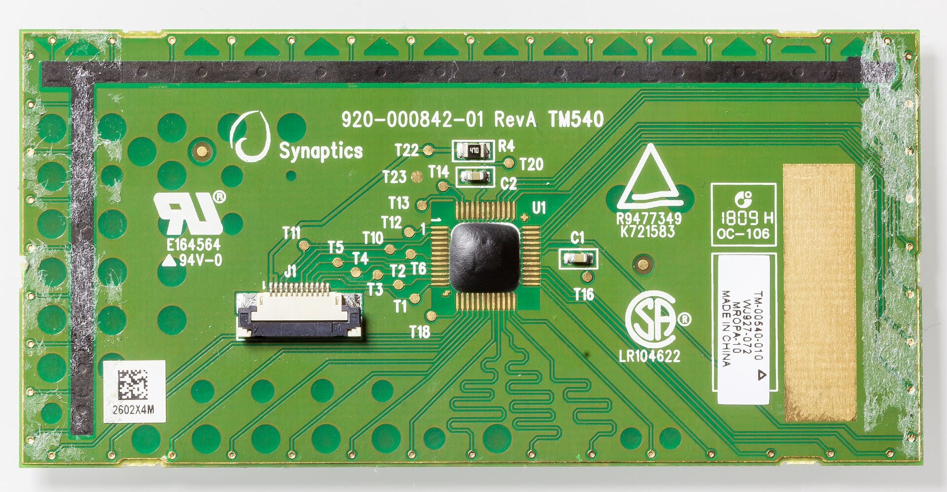 A green Synaptics touchpad controller board, the Synaptics logo printed beside its chip.