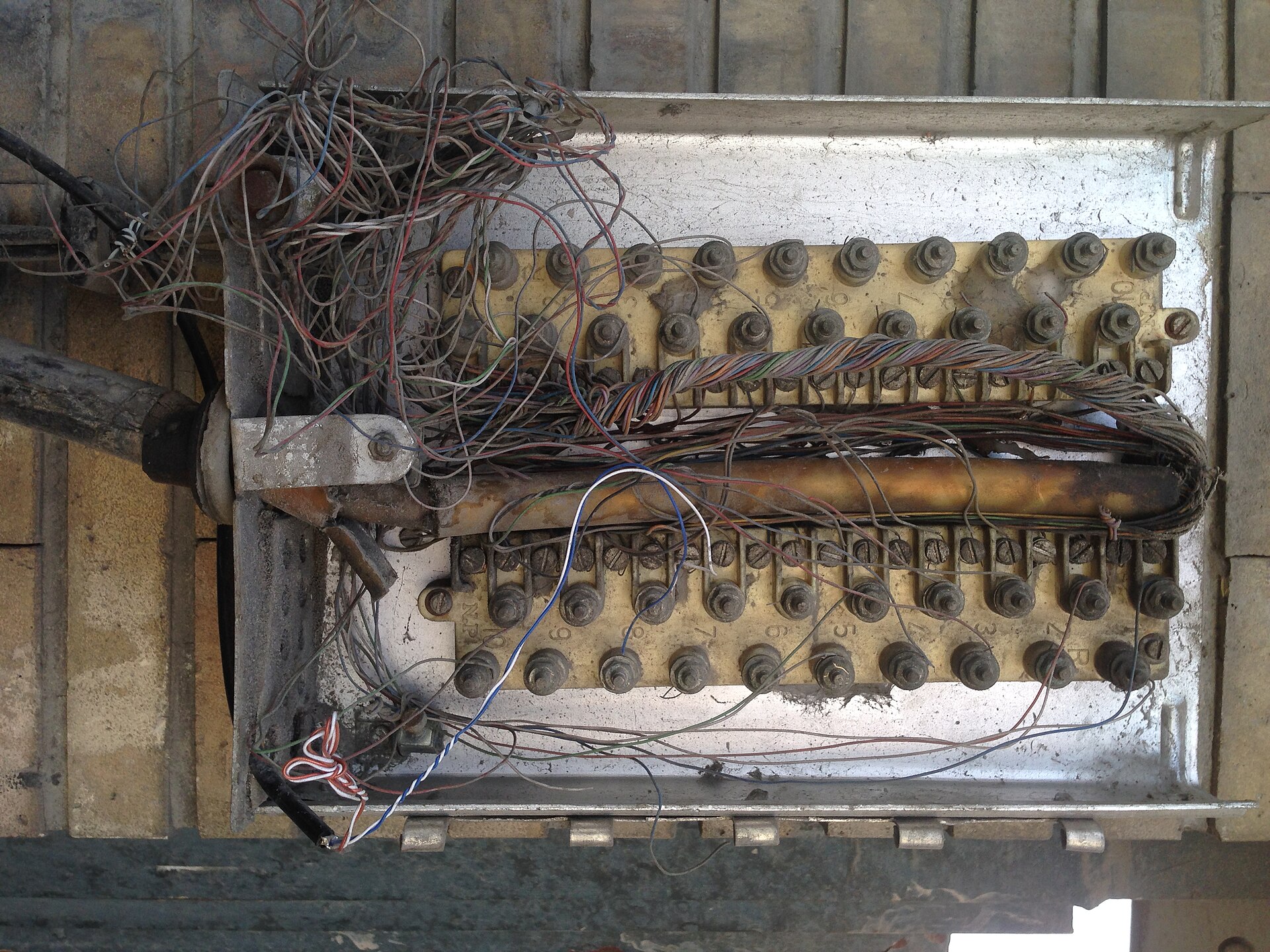 Copper telephone pairs terminating on rows of screw terminals inside a weathered wall-mounted distribution box