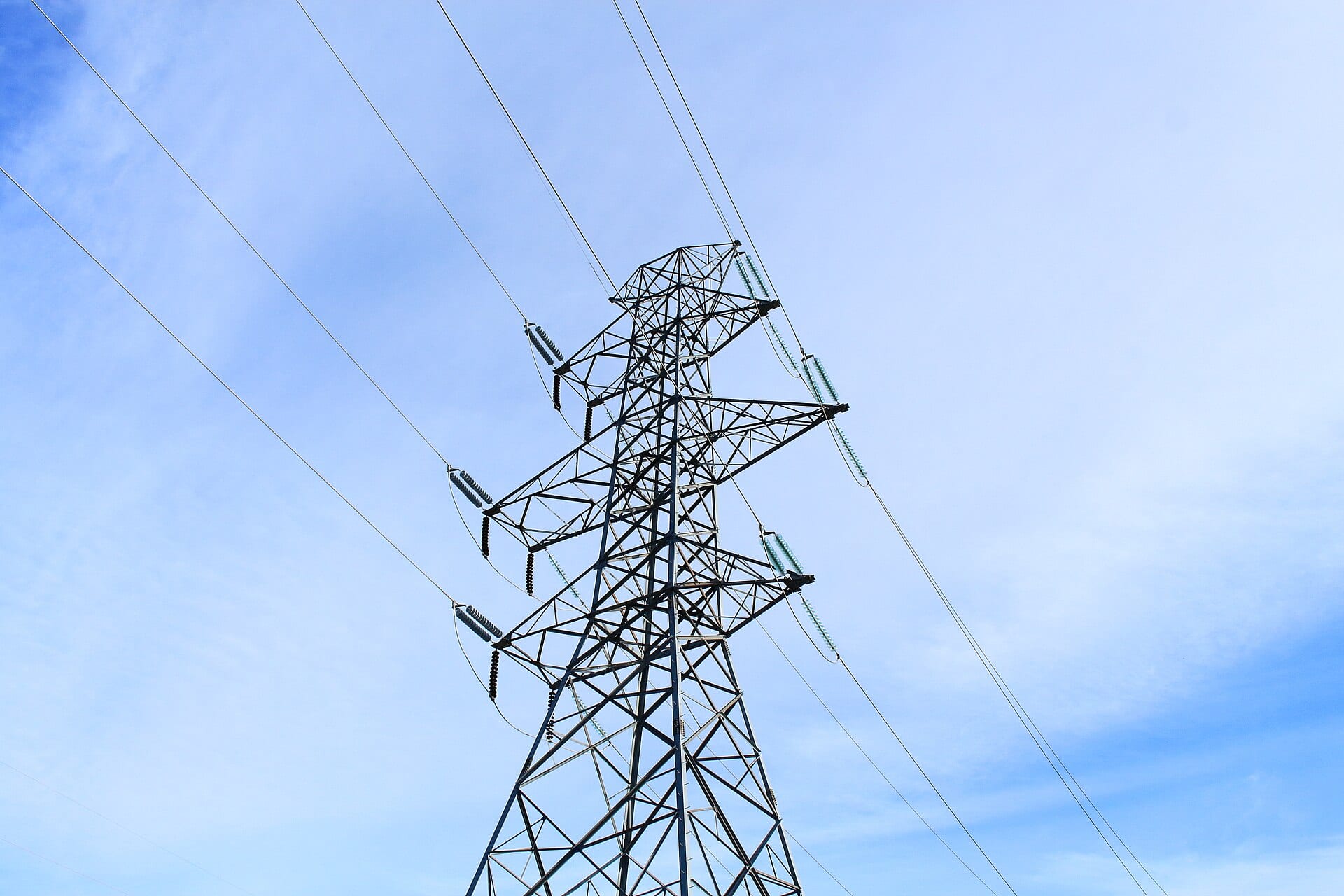 A high-voltage transmission tower against a blue sky, seen from below
