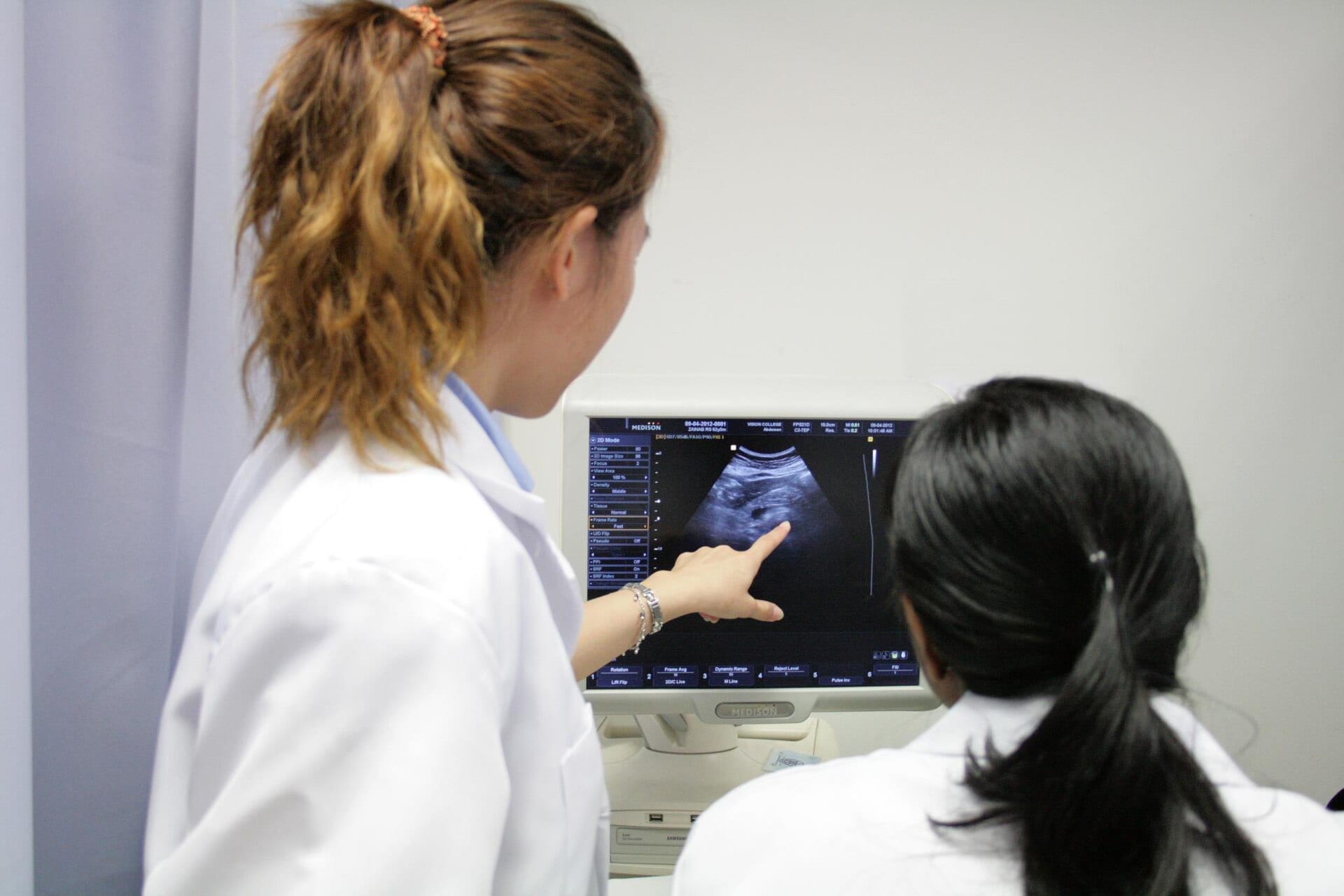 A sonographer points at an ultrasound image on a monitor while a colleague watches
