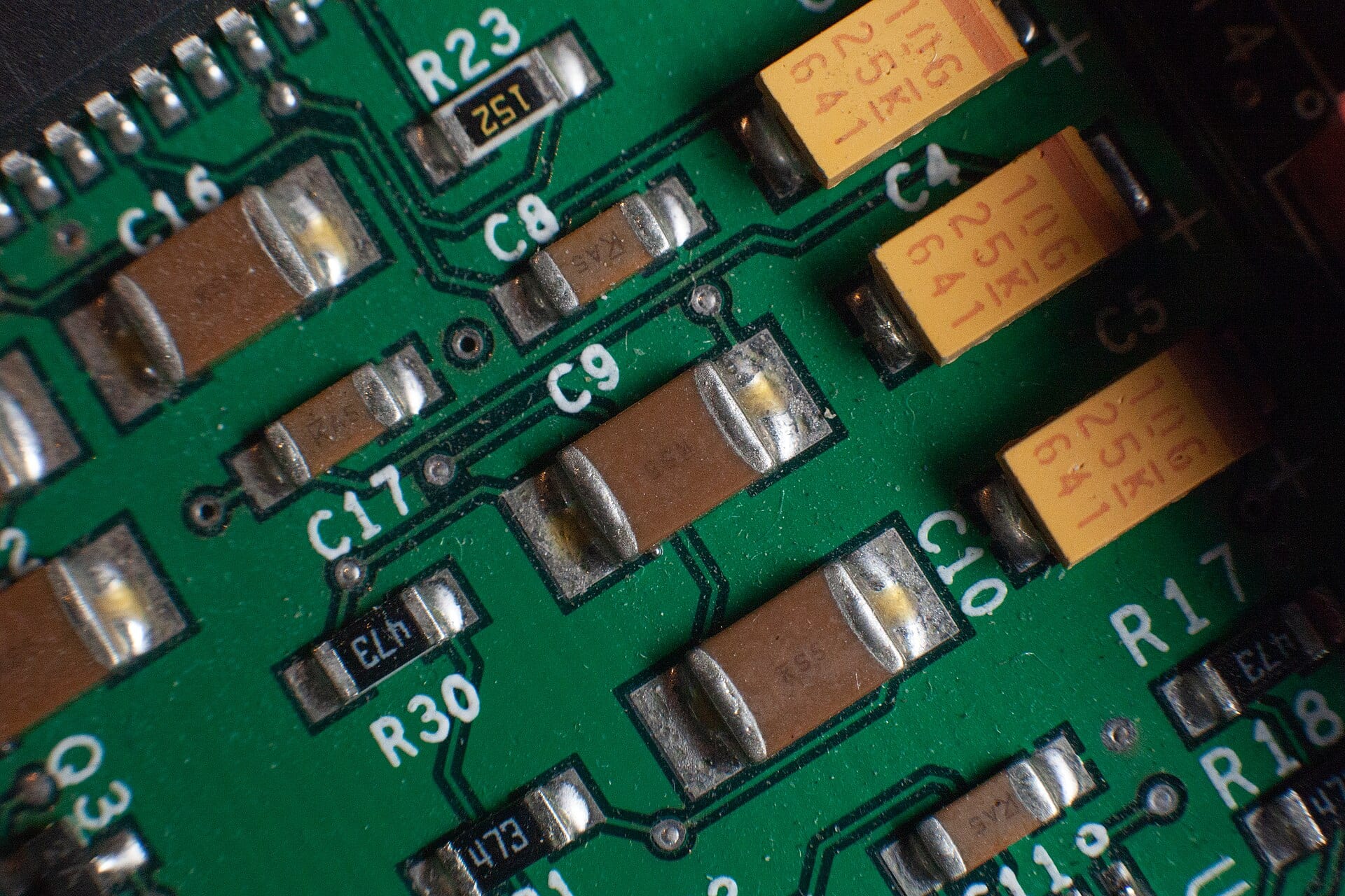 Close-up of multilayer ceramic capacitors and other components soldered onto a green printed circuit board.