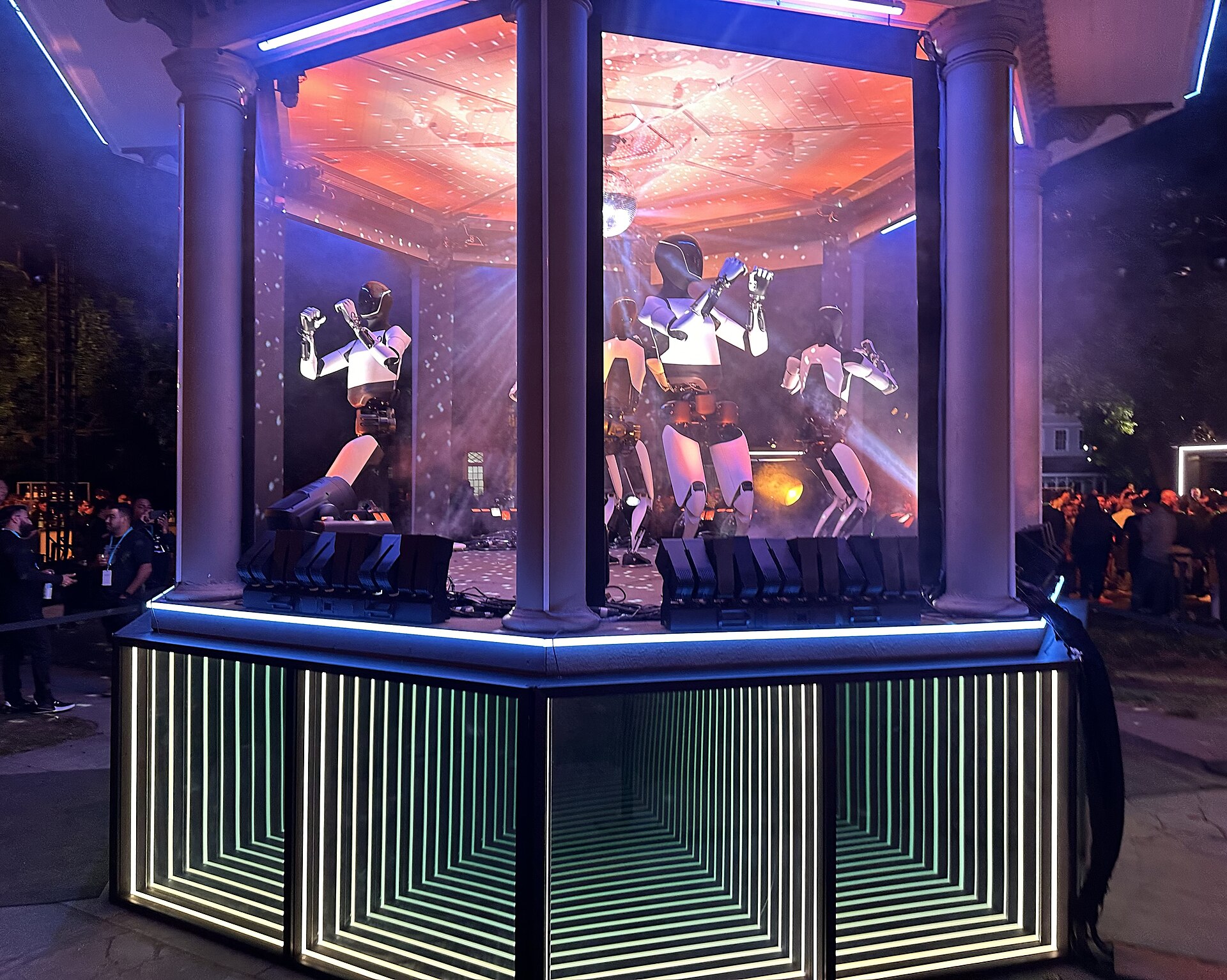A fleet of Tesla Optimus robots performing on a lit stage at Tesla's 10/10 Robotaxi event in October 2024