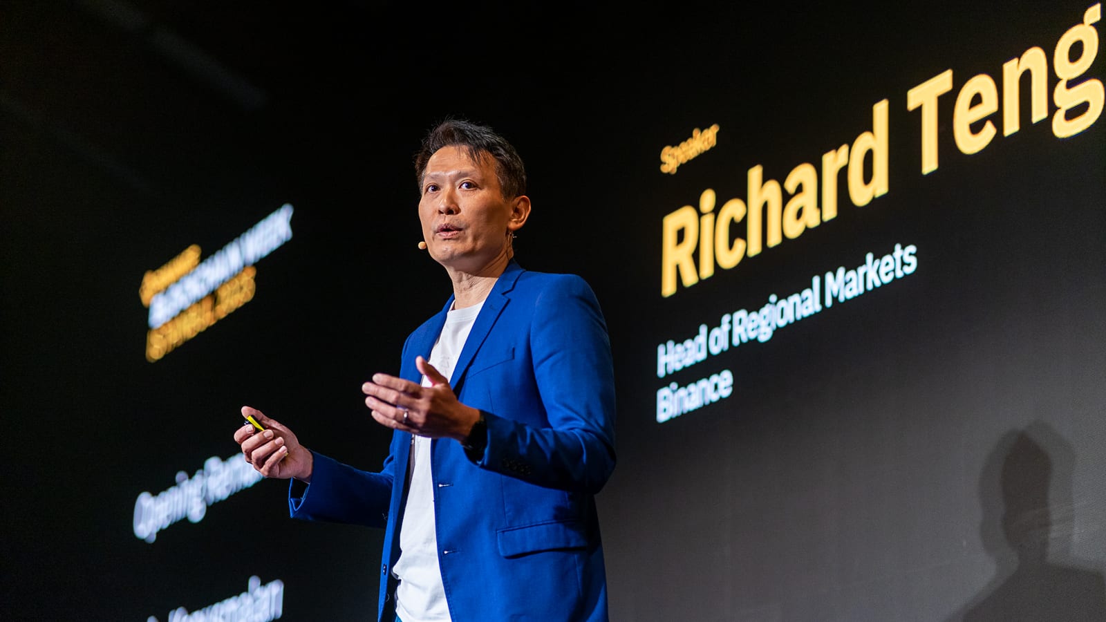Binance CEO Richard Teng speaking on stage at Binance Blockchain Week 2023 in Istanbul, with his name and the Binance logo projected on screens behind him.