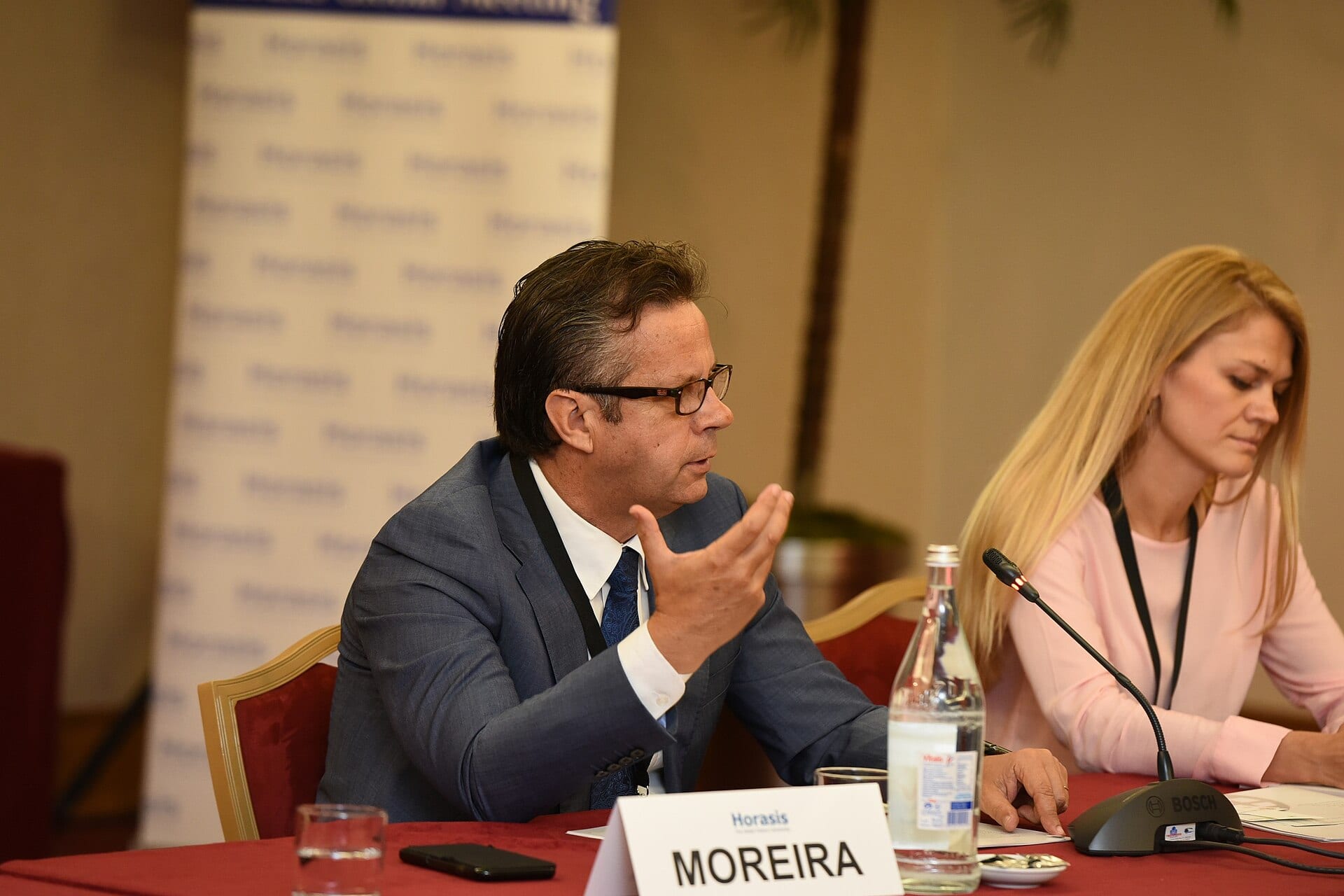 Carlos Moreira speaks at a conference panel, seated behind a name plate reading Moreira