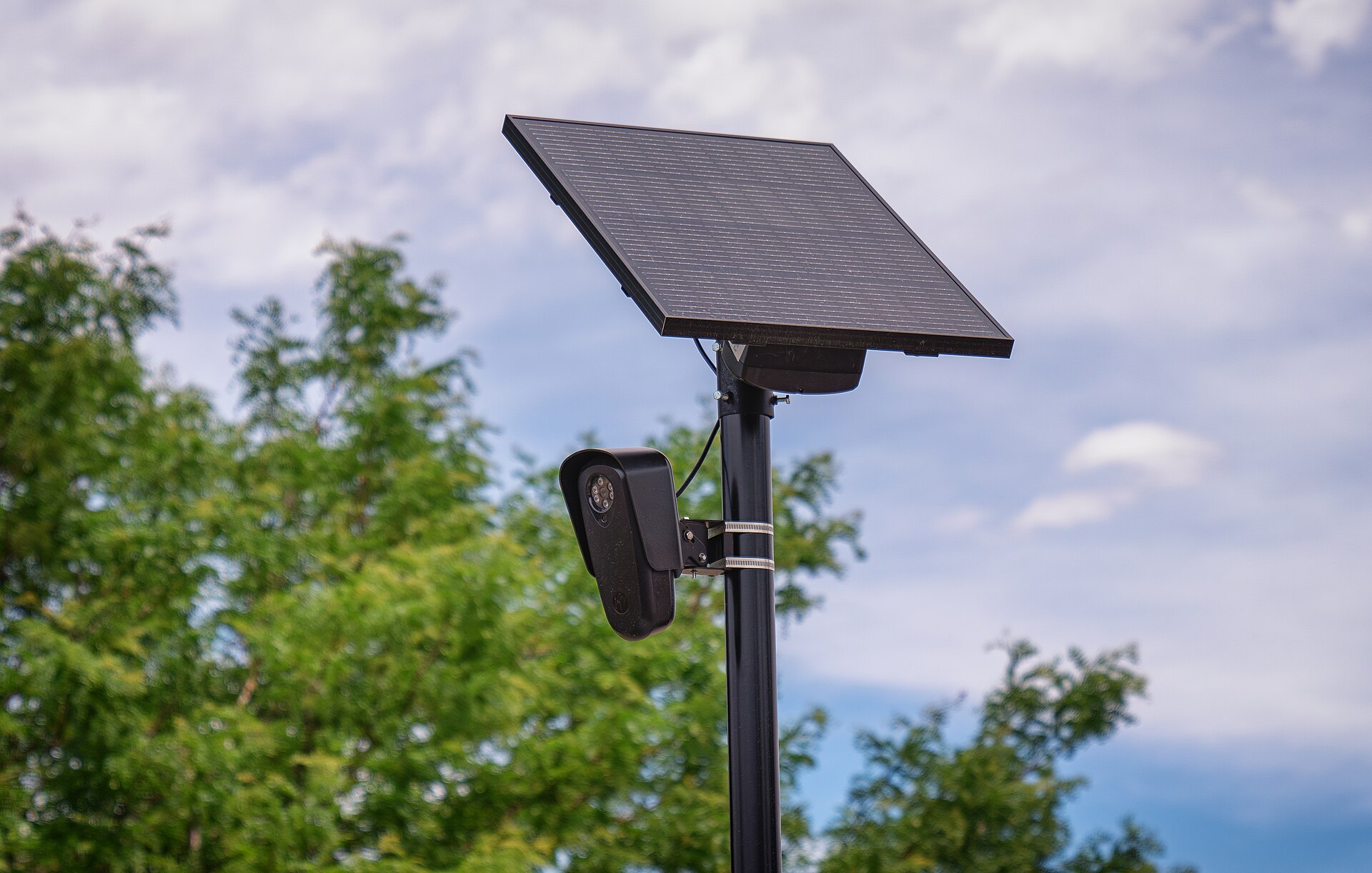 A Flock Safety automatic license plate reader camera mounted on a pole, with its solar panel overhead.