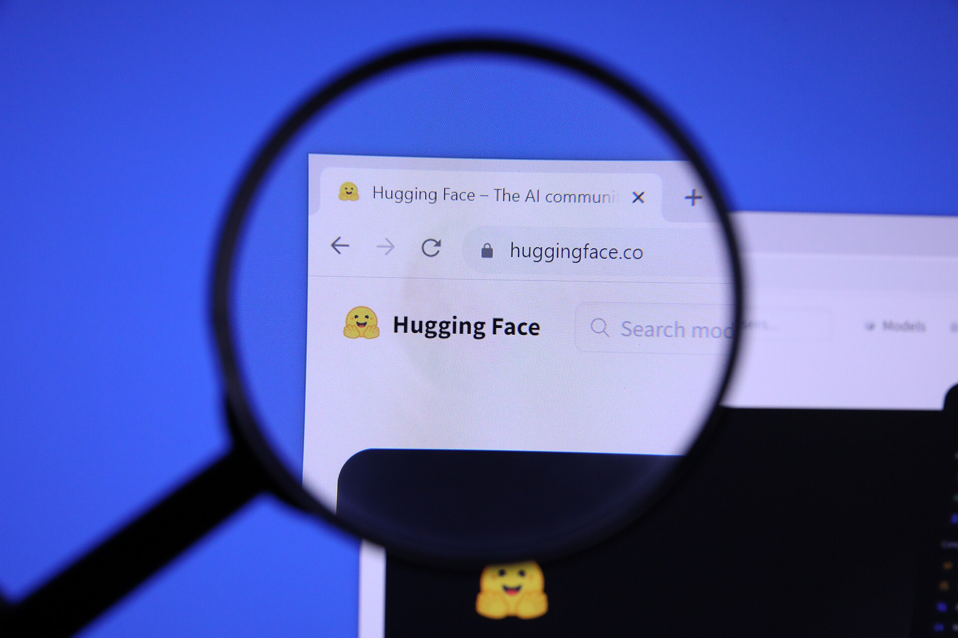 The Hugging Face homepage on a screen, seen through a magnifying glass