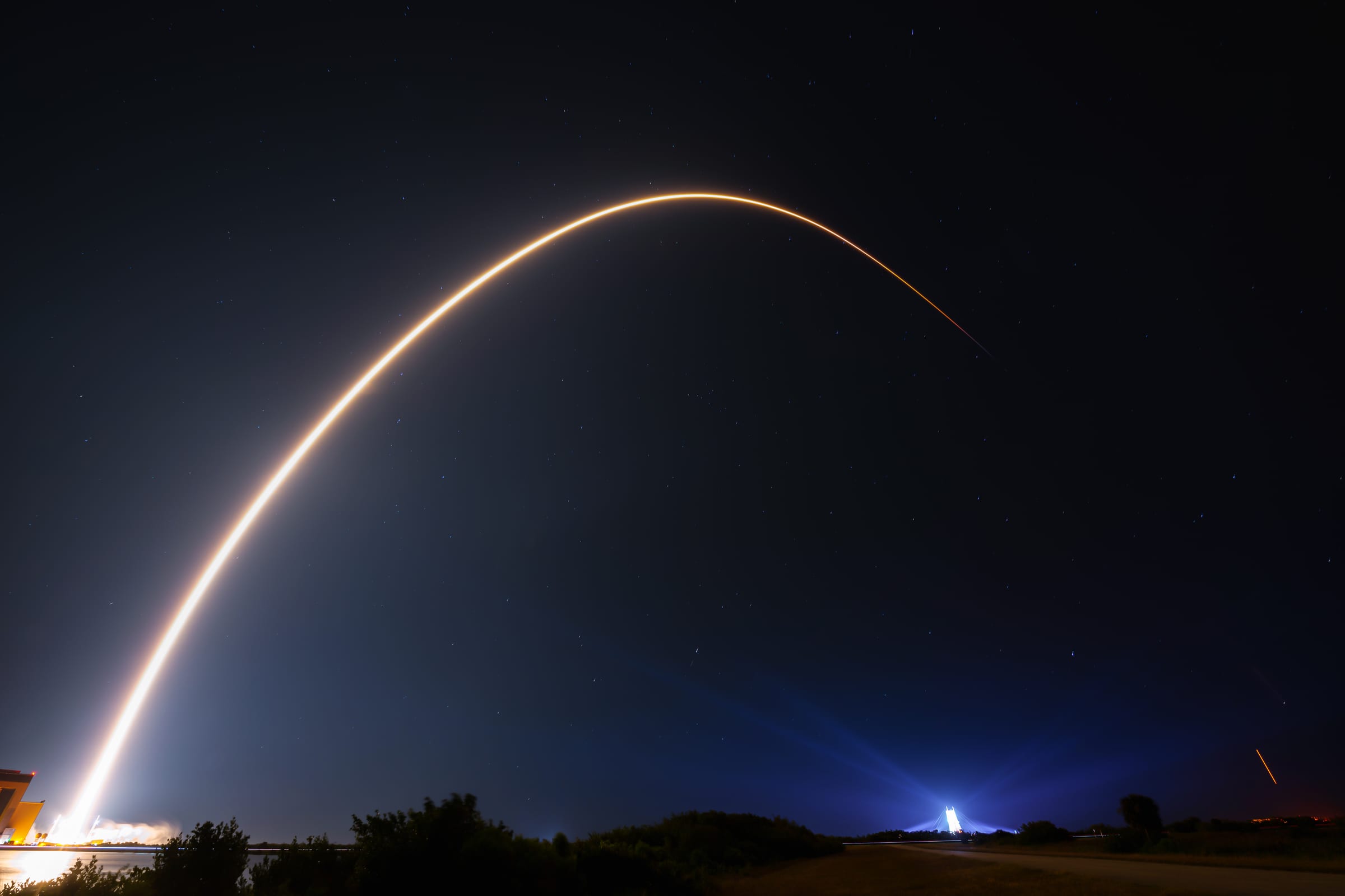 Long-exposure night photograph of a Falcon 9 Starlink launch from Cape Canaveral, the rocket's bright arc crossing a starry sky