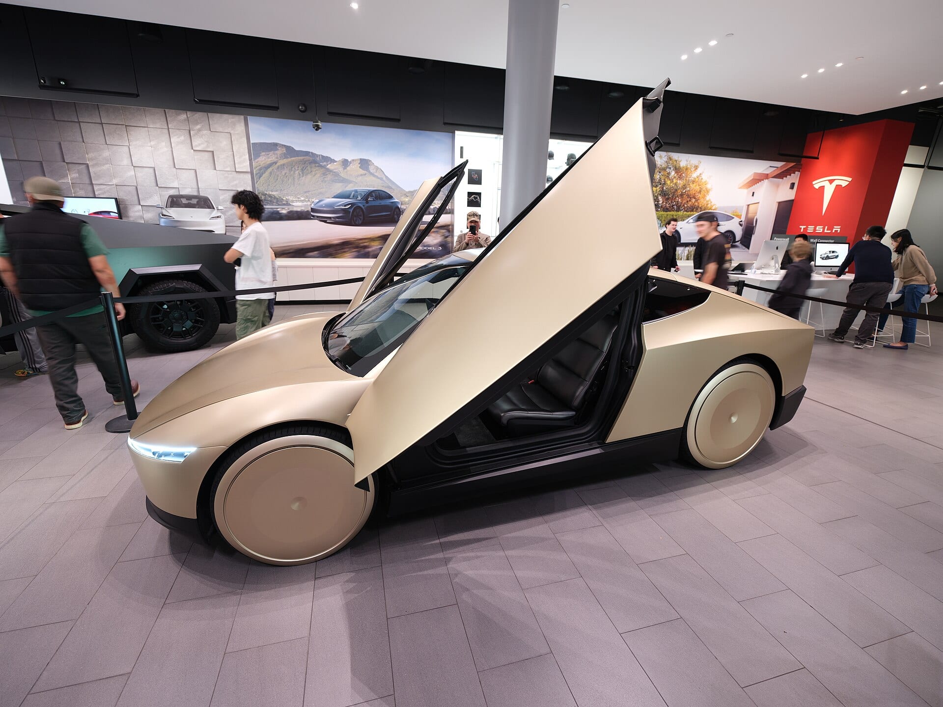 A gold Tesla Cybercab with upward-opening doors on display, a two-seat car with no steering wheel