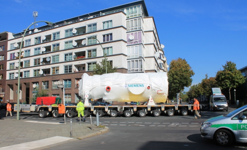 A Siemens gas turbine wrapped for transport moves through a Berlin street on a multi-axle heavy-haul trailer.