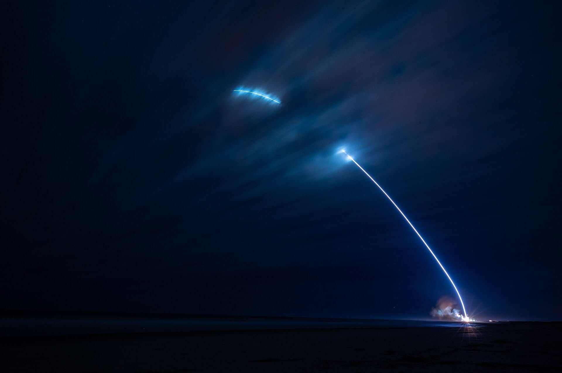 New Glenn lifts off at night from Space Launch Complex 36, a long exposure catching the rocket's ascent and the booster's return burn as two arcs over the Atlantic