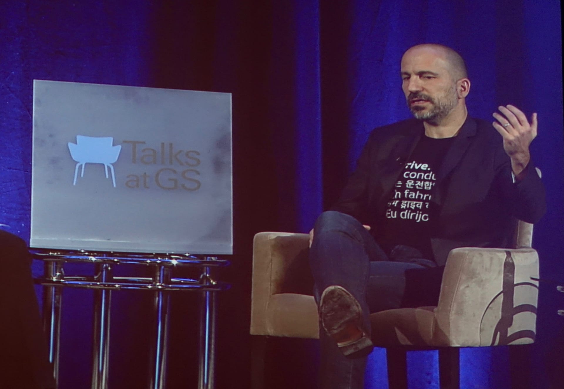 Uber chief executive Dara Khosrowshahi seated onstage, gesturing with one hand while speaking at a Goldman Sachs technology conference.