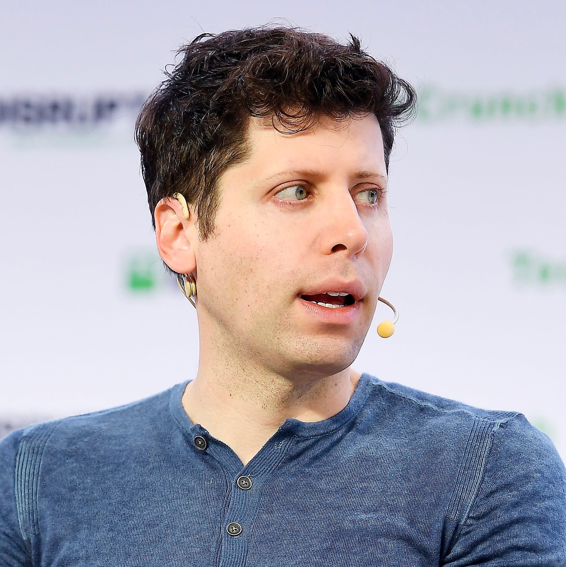 Sam Altman speaking on stage with a headset microphone