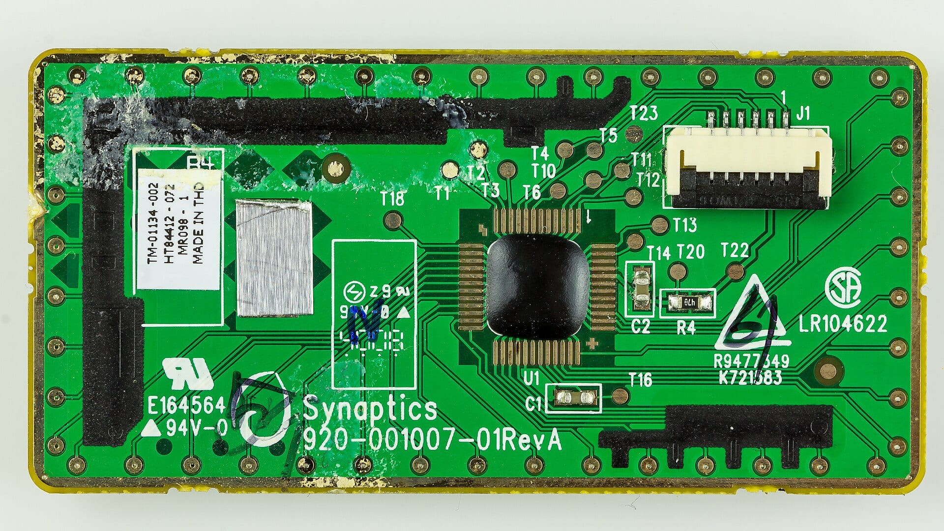 Close-up of a green circuit board for a Synaptics touchpad controller, part number 920-001007-01, with the Synaptics logo printed on the board.
