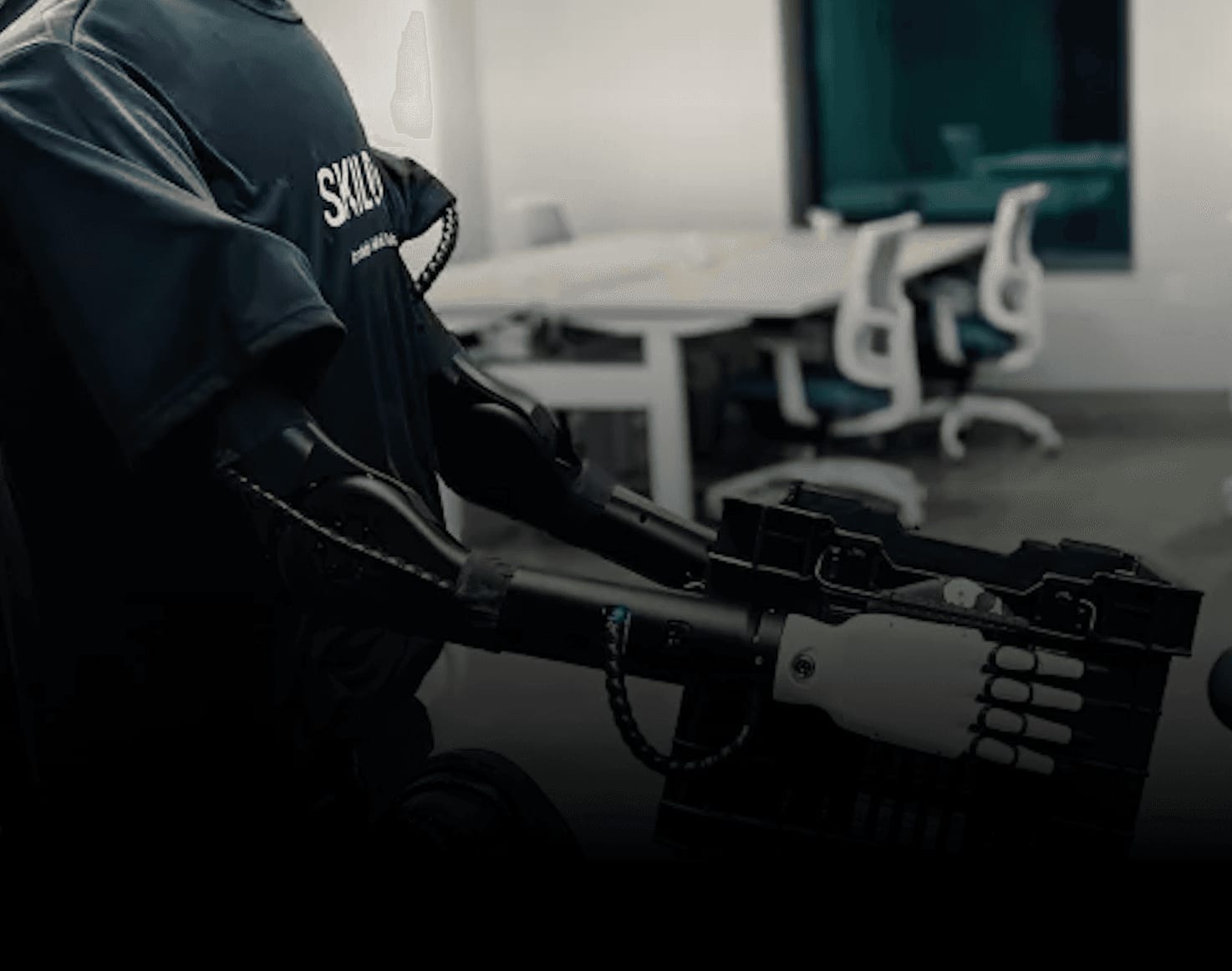A Skild AI mobile manipulation robot with a Skild-branded shirt carrying a plastic tote through an office