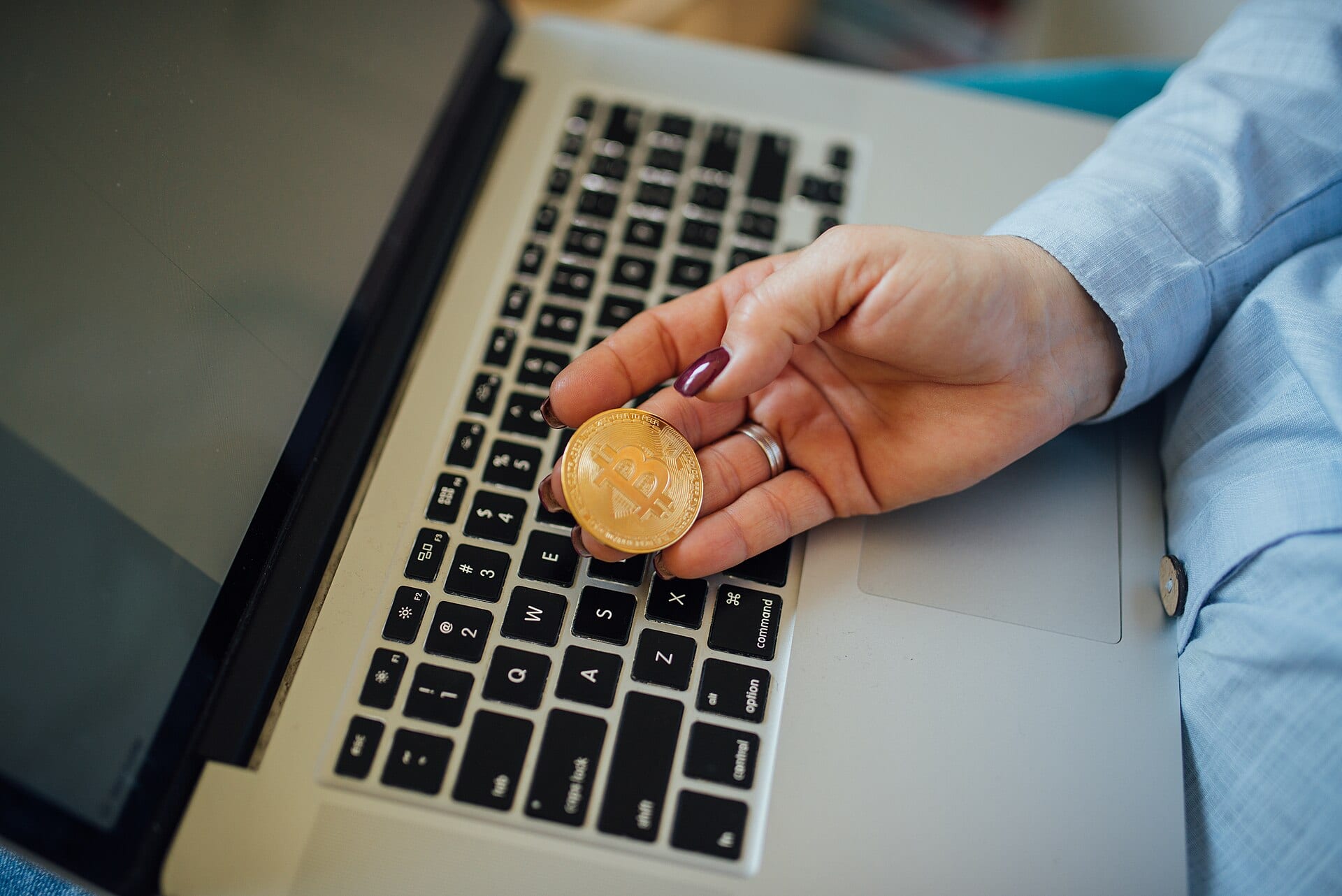 A hand holding a physical bitcoin token above a laptop keyboard