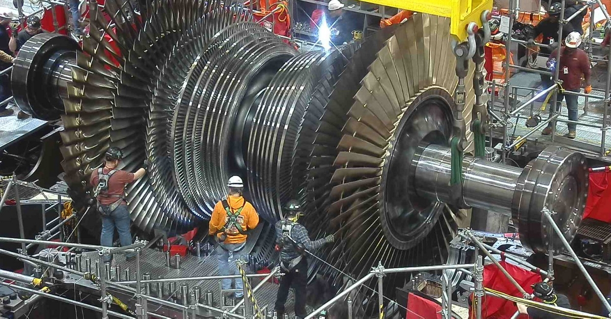 Workers guide a large steam turbine into place during a power plant upgrade