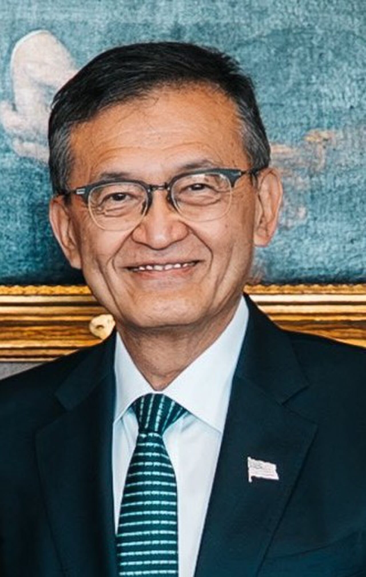 Intel chief executive Lip-Bu Tan in a dark suit and striped tie, smiling, at the US Department of Commerce in 2025