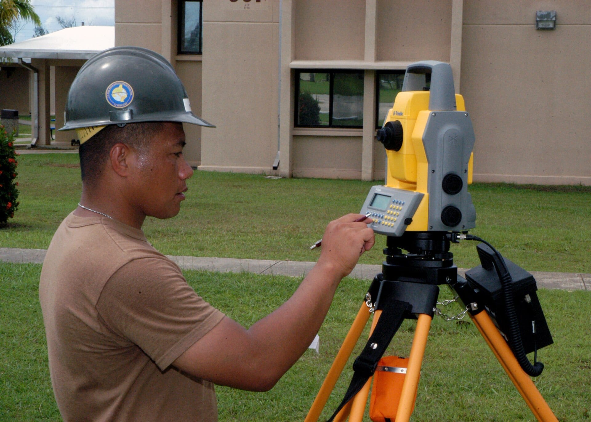 An engineering aide operates a yellow Trimble total station surveying instrument on a tripod.