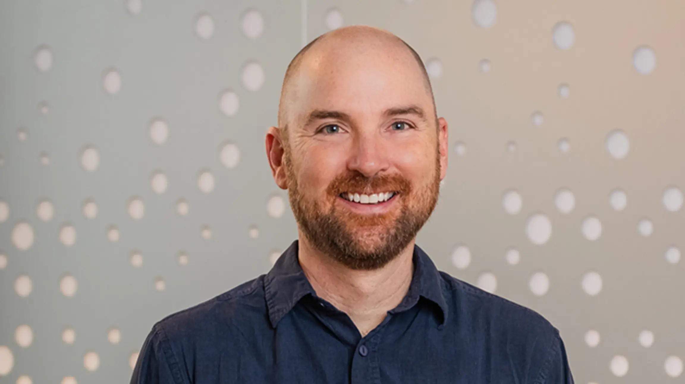 Ed Hallen, co-founder and chief product officer of Klaviyo, smiling in a navy shirt against a grey wall with a pattern of circles