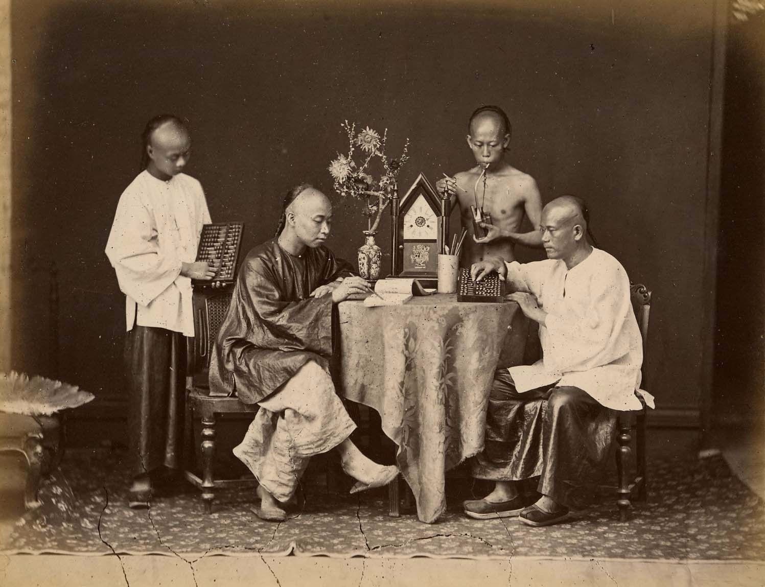 Nineteenth-century photograph of four accountants at a table with abacuses, ledgers and a clock
