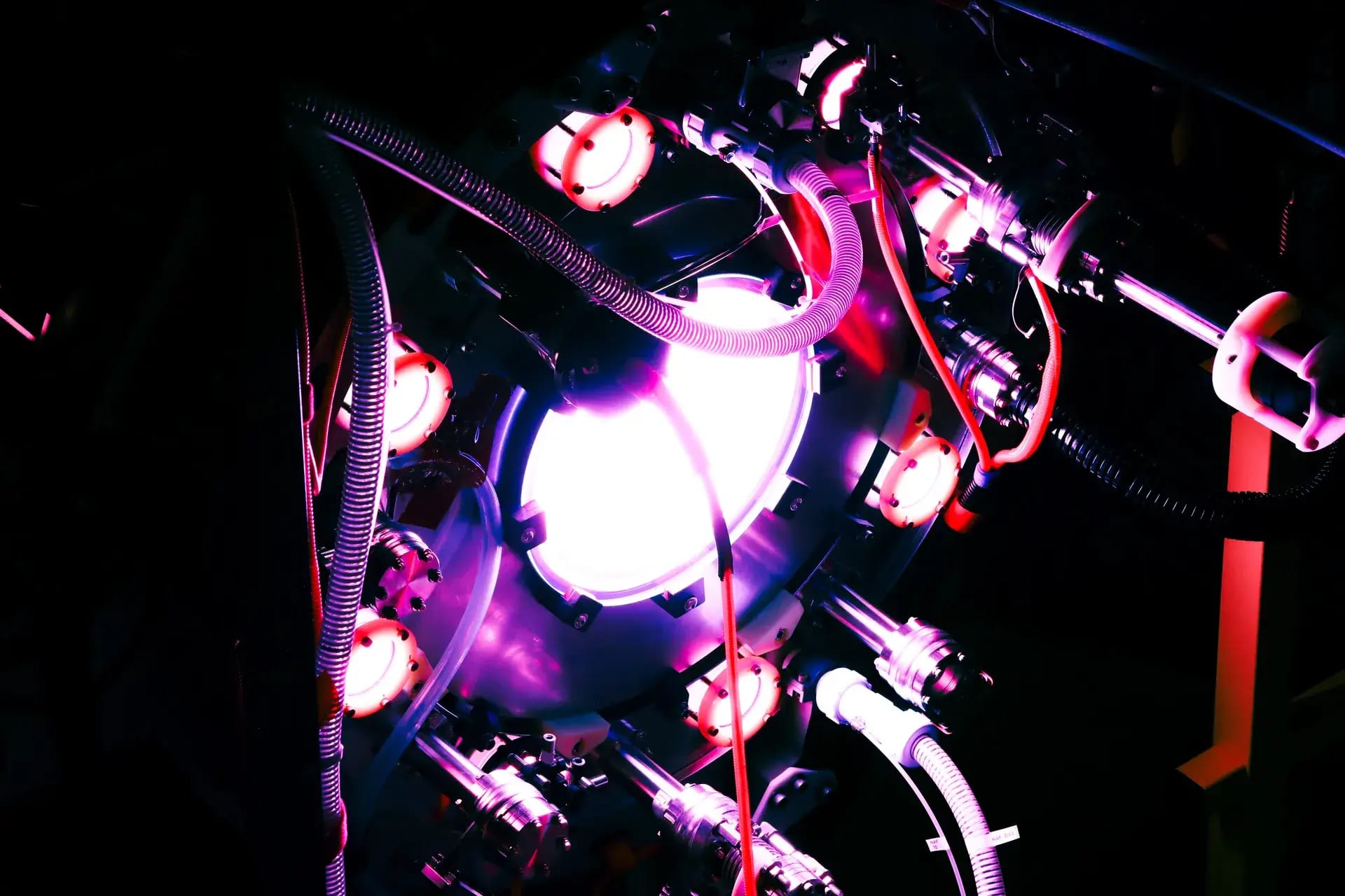 Helion's Polaris fusion prototype, close up, with glowing ports, cables and high-voltage plumbing against a dark background
