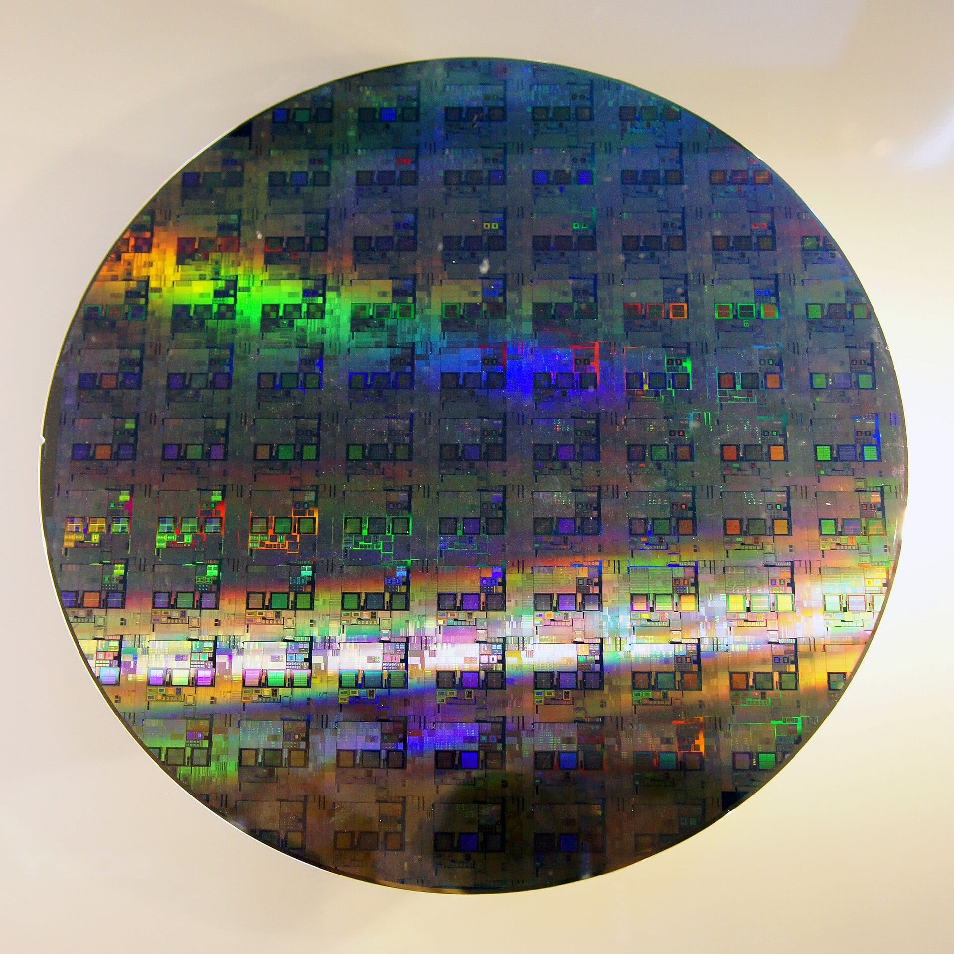 A 12-inch silicon wafer covered in processed dies, iridescent under light