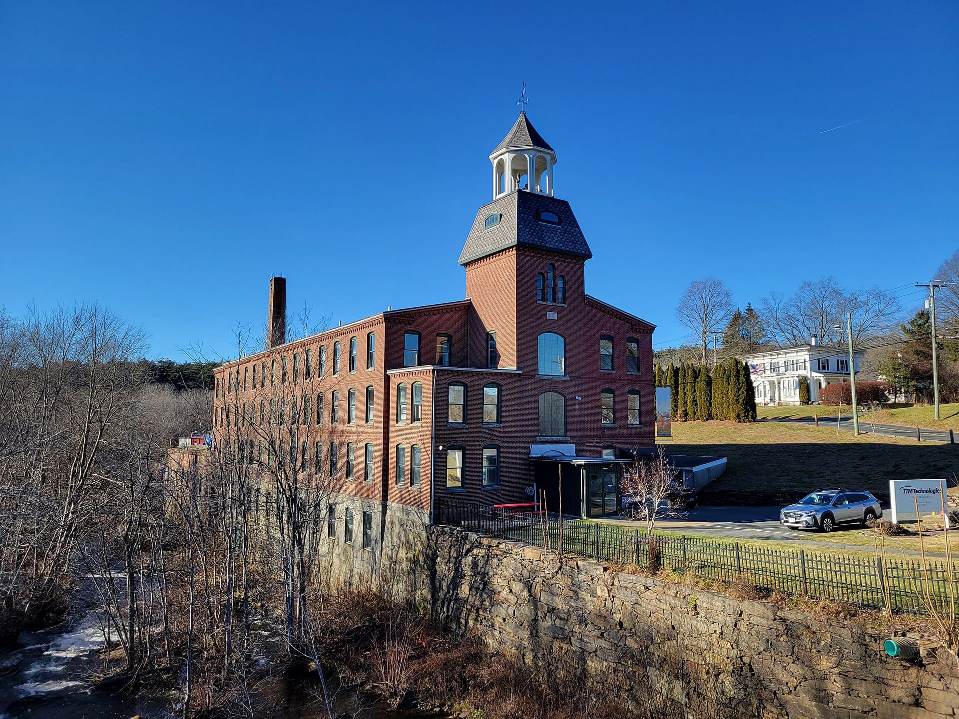 TTM Technologies' Stafford Division plant in Stafford, Connecticut, a red brick mill building beside a river