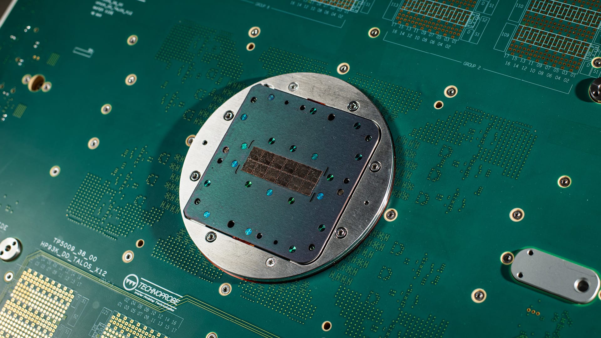 A Technoprobe probe card mounted on its green test interface board, contact pads and connectors visible around the central card