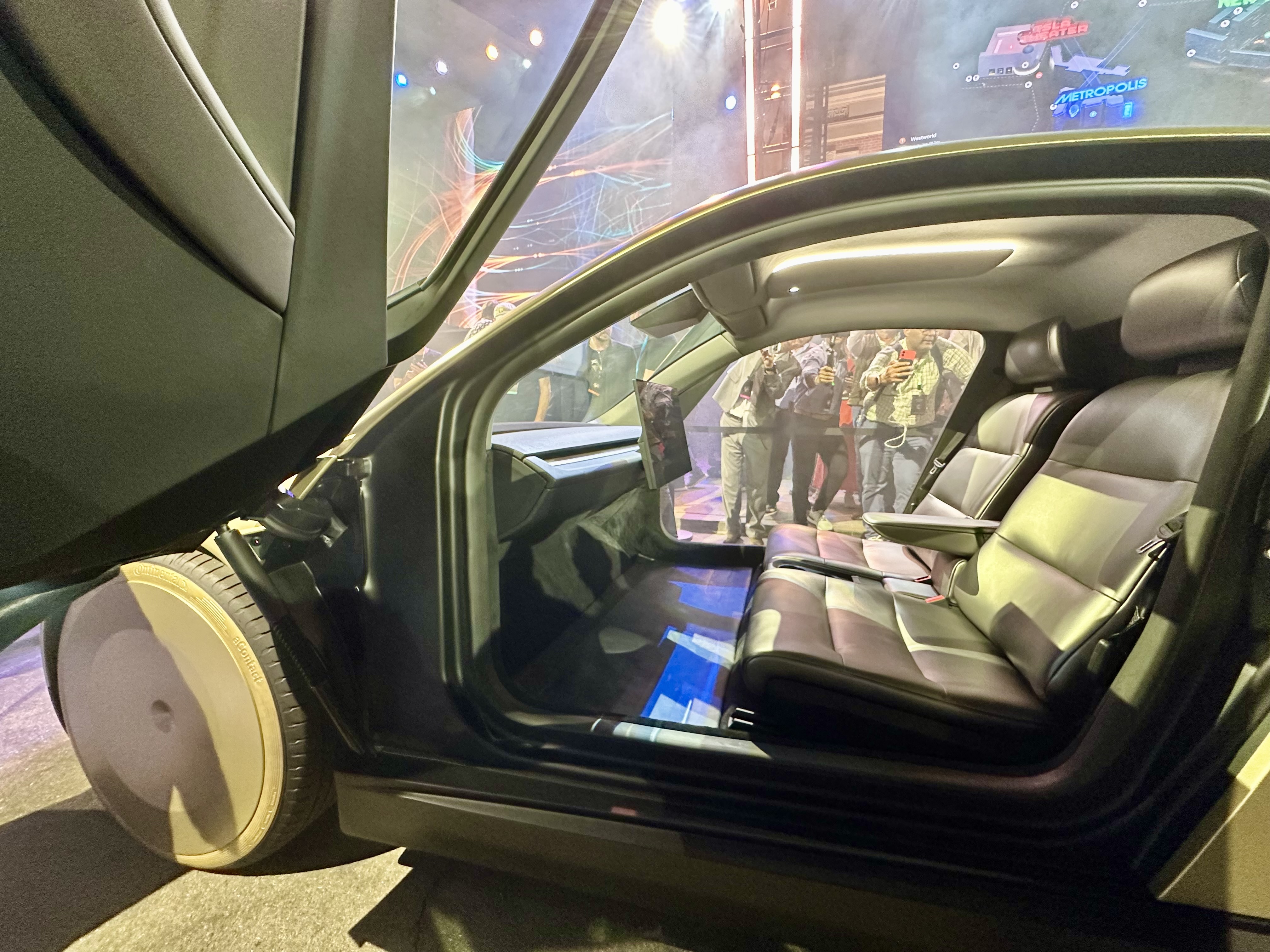 The Cybercab's two-seat cabin, photographed through its open butterfly door: a bench seat and a central screen, with no steering wheel or pedals.
