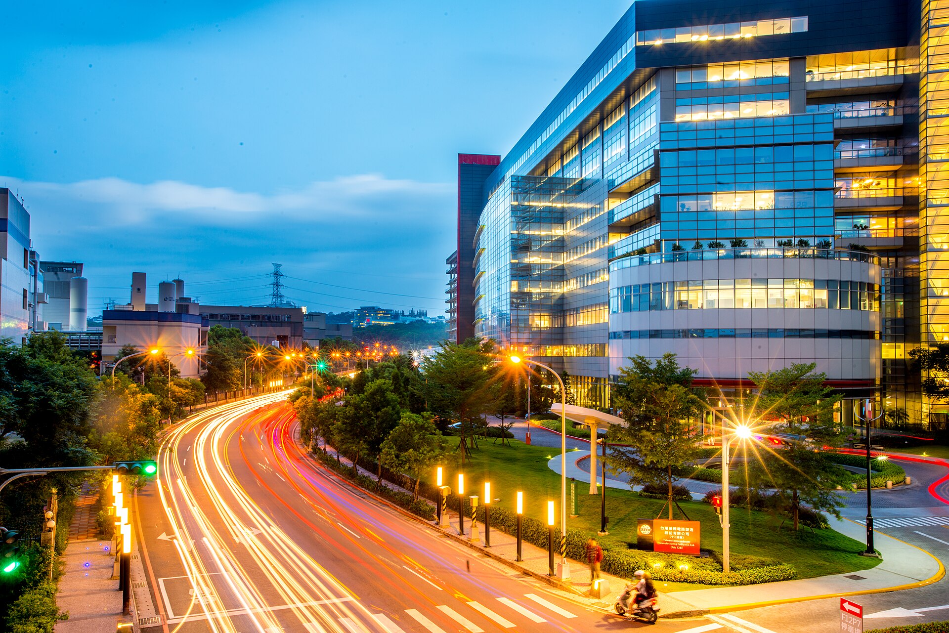 TSMC's Fab 12B building at dusk in Hsinchu, Taiwan, its glass facade lit above a road of light trails