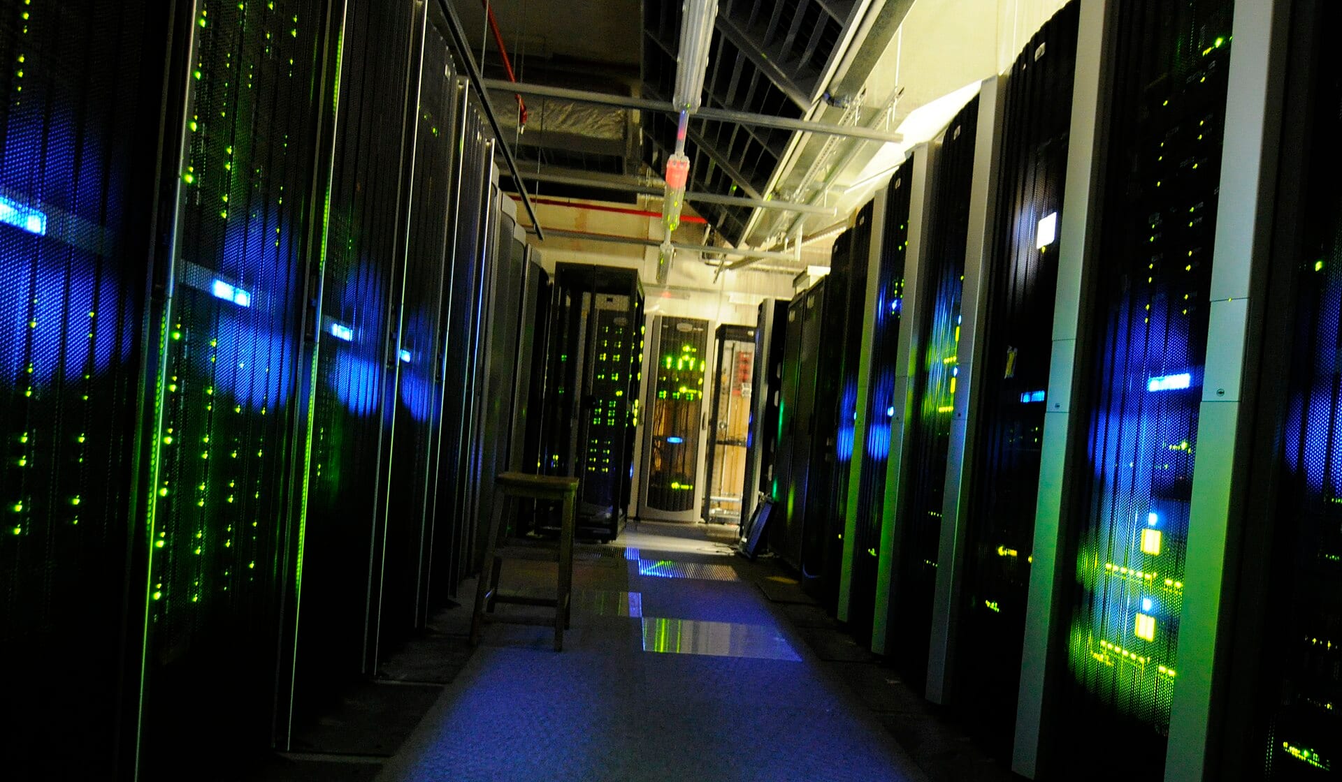 Rows of dark server racks with blue and green indicator lights along an aisle in the server room at The National Archives, London.