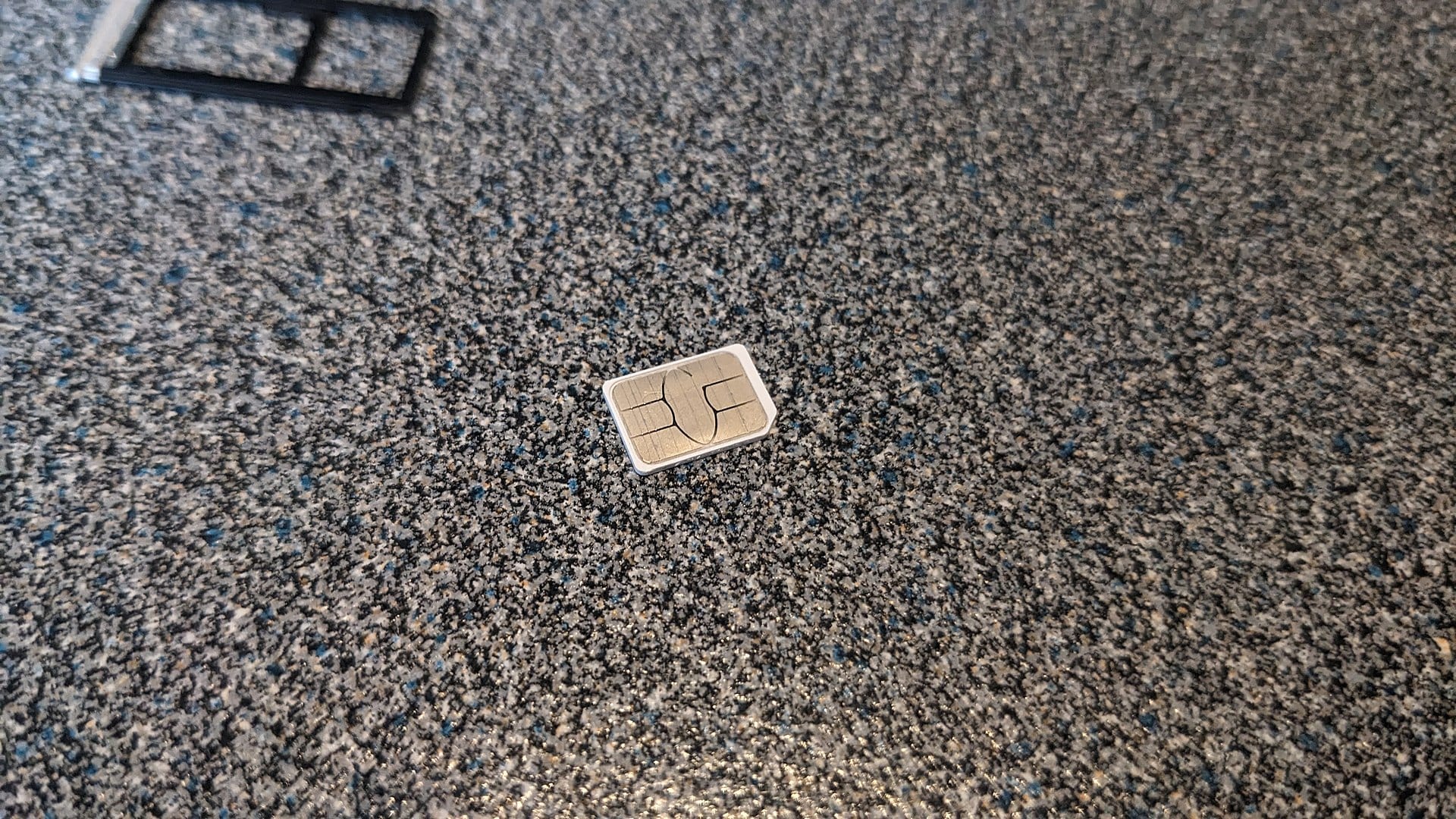 A nano SIM card lying on a granite counter, the physical card that eSIM technology installed inside an app replaces