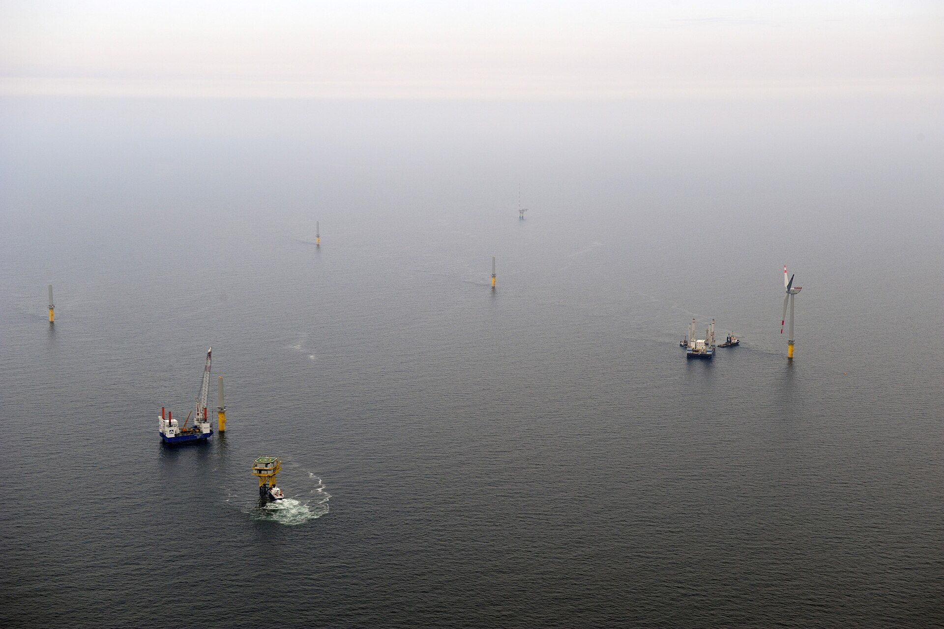 Aerial view of the alpha ventus offshore wind farm under construction in the North Sea, with turbines, foundations and service vessels in grey water