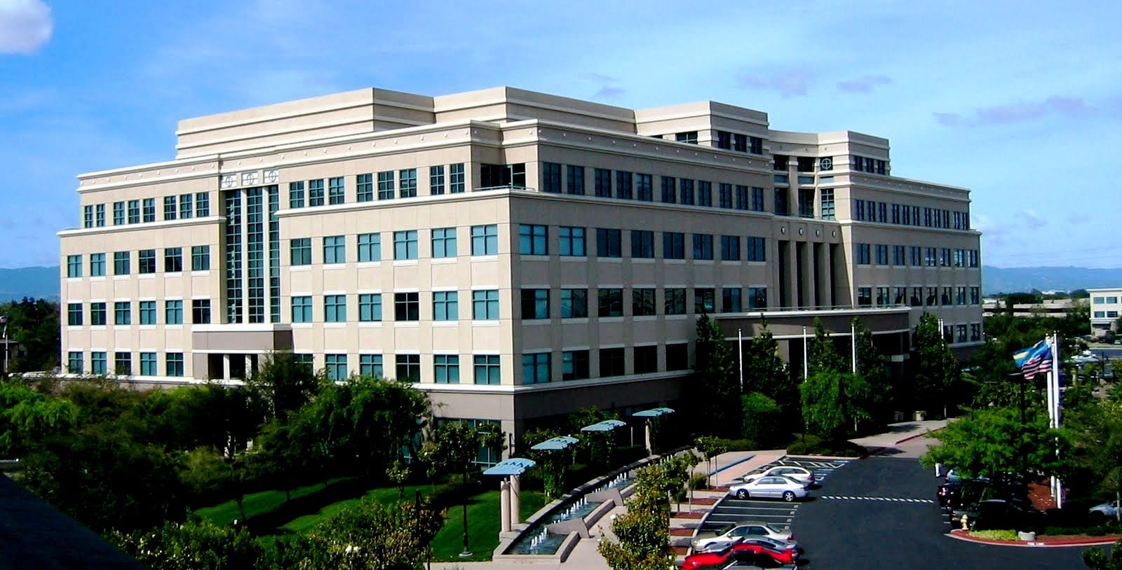 The Building 10 office tower at Cisco's San Jose main campus under a blue sky, with a flag in the foreground