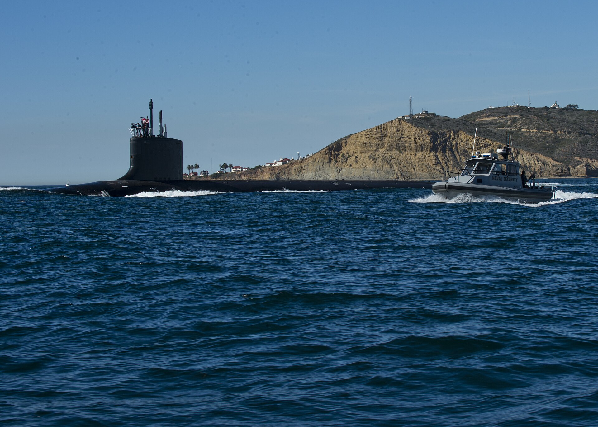 A Virginia-class attack submarine running on the surface off San Diego, escorted by a Navy security boat