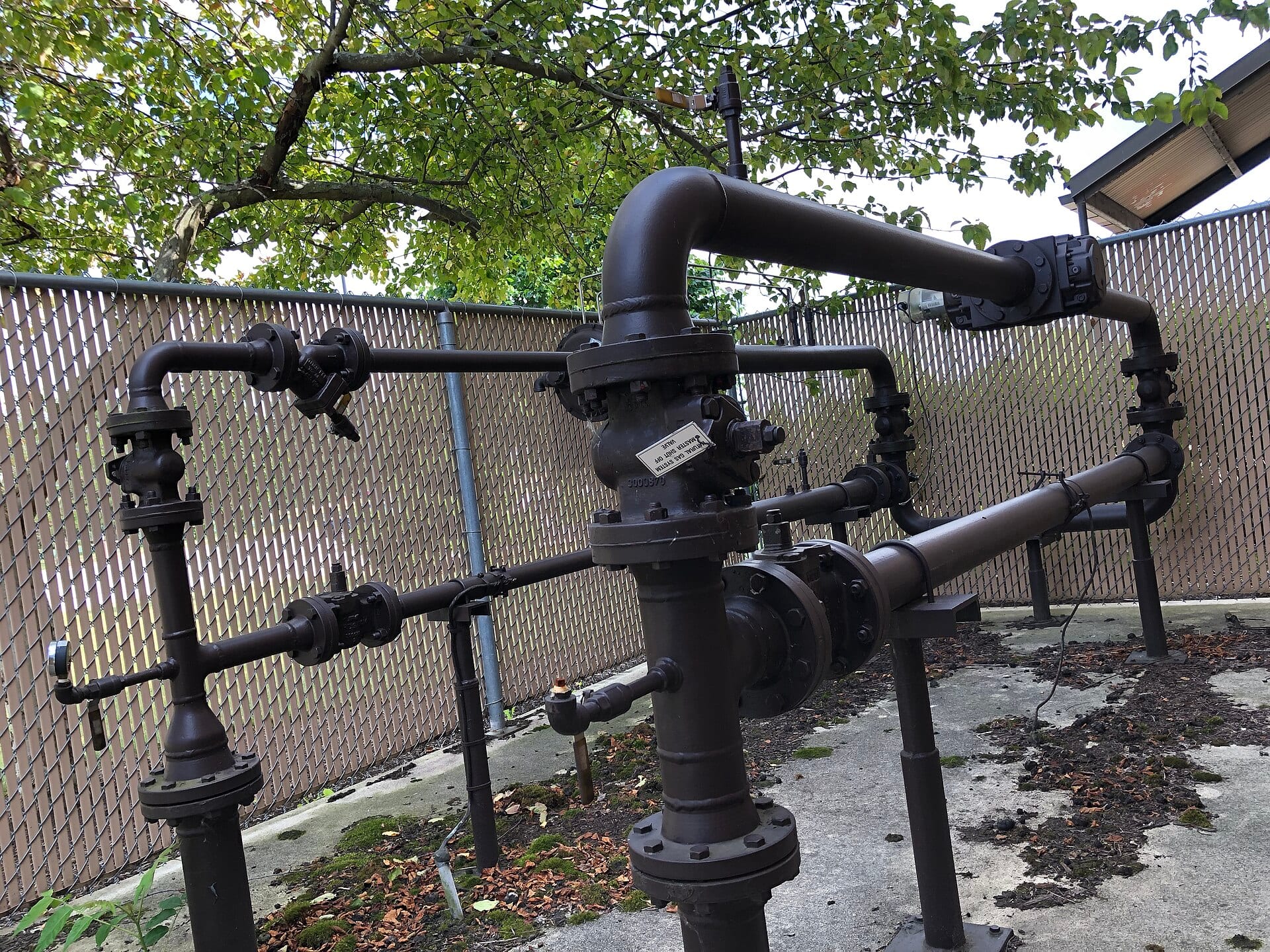 Pipes and valves at an above-ground natural gas pipeline station, with a chain-link fence behind
