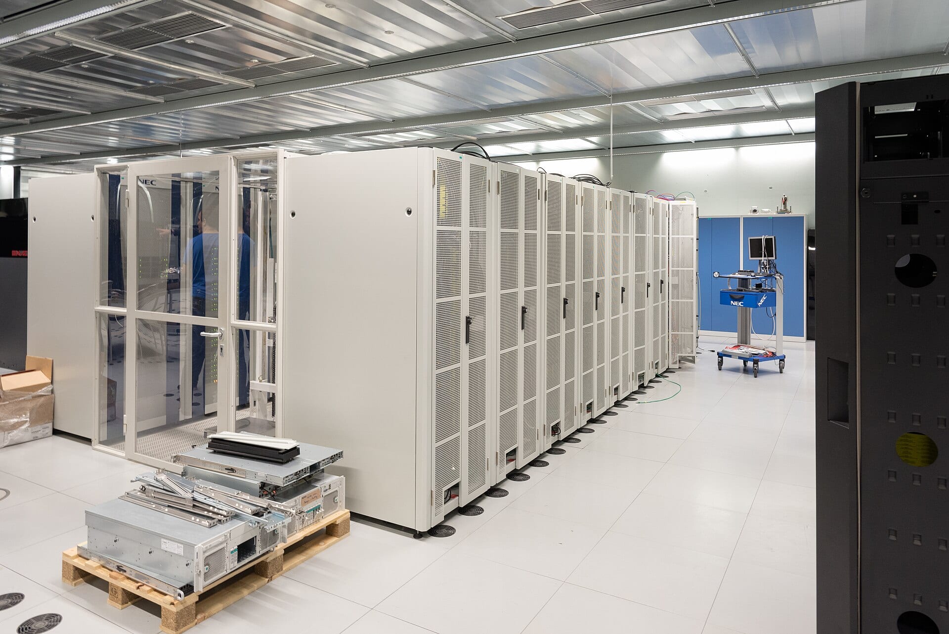 A row of compute cabinets being installed in a data hall, with rack-mount hardware still on a pallet in the foreground