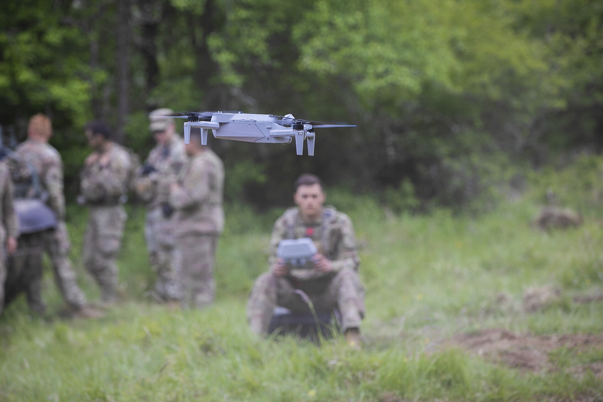 A Skydio X10 in flight as a soldier flies it from a handheld controller