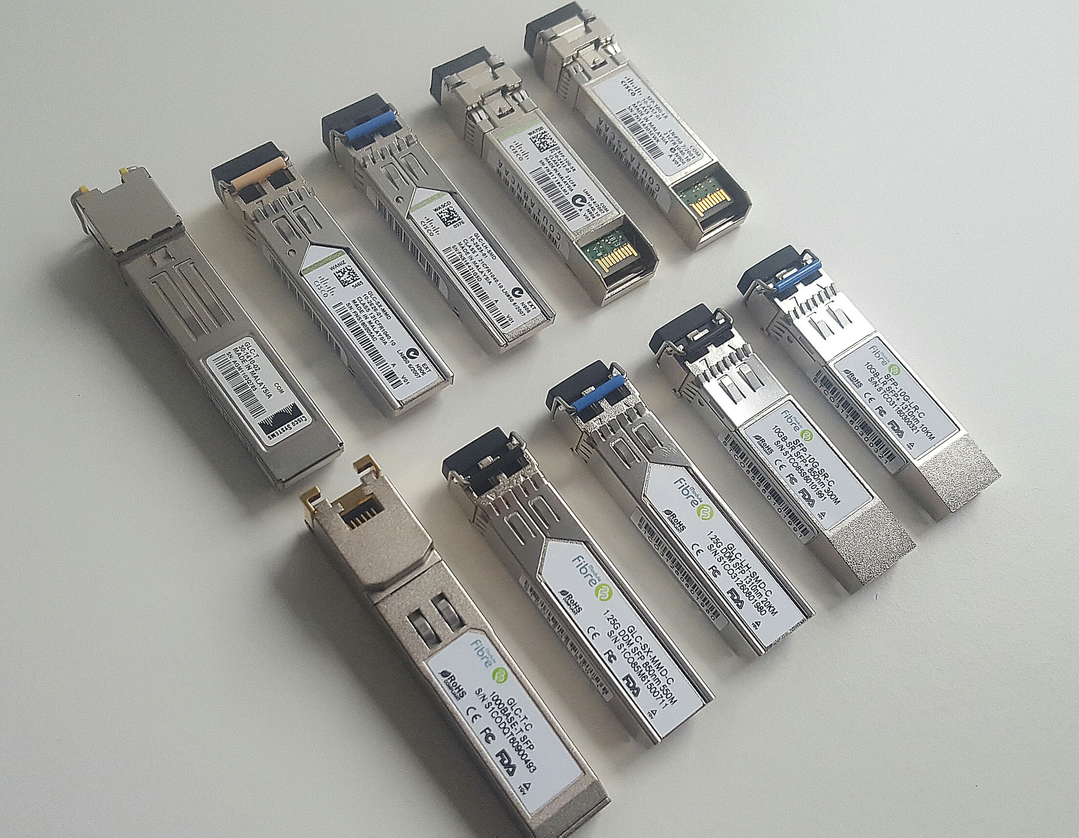 A row of pluggable SFP optical transceiver modules, Cisco-branded and compatible versions, arranged on a flat surface