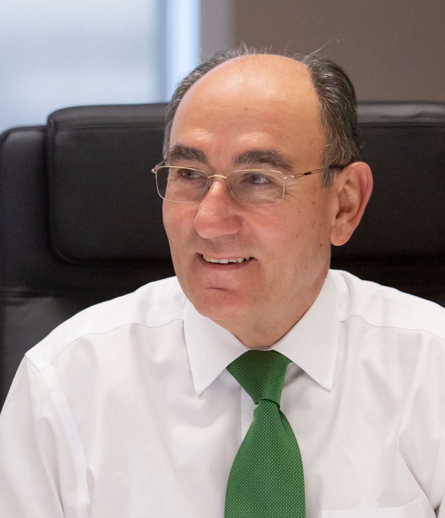 Iberdrola chairman Ignacio Sánchez Galán seated at a conference table, wearing a white shirt and green tie.