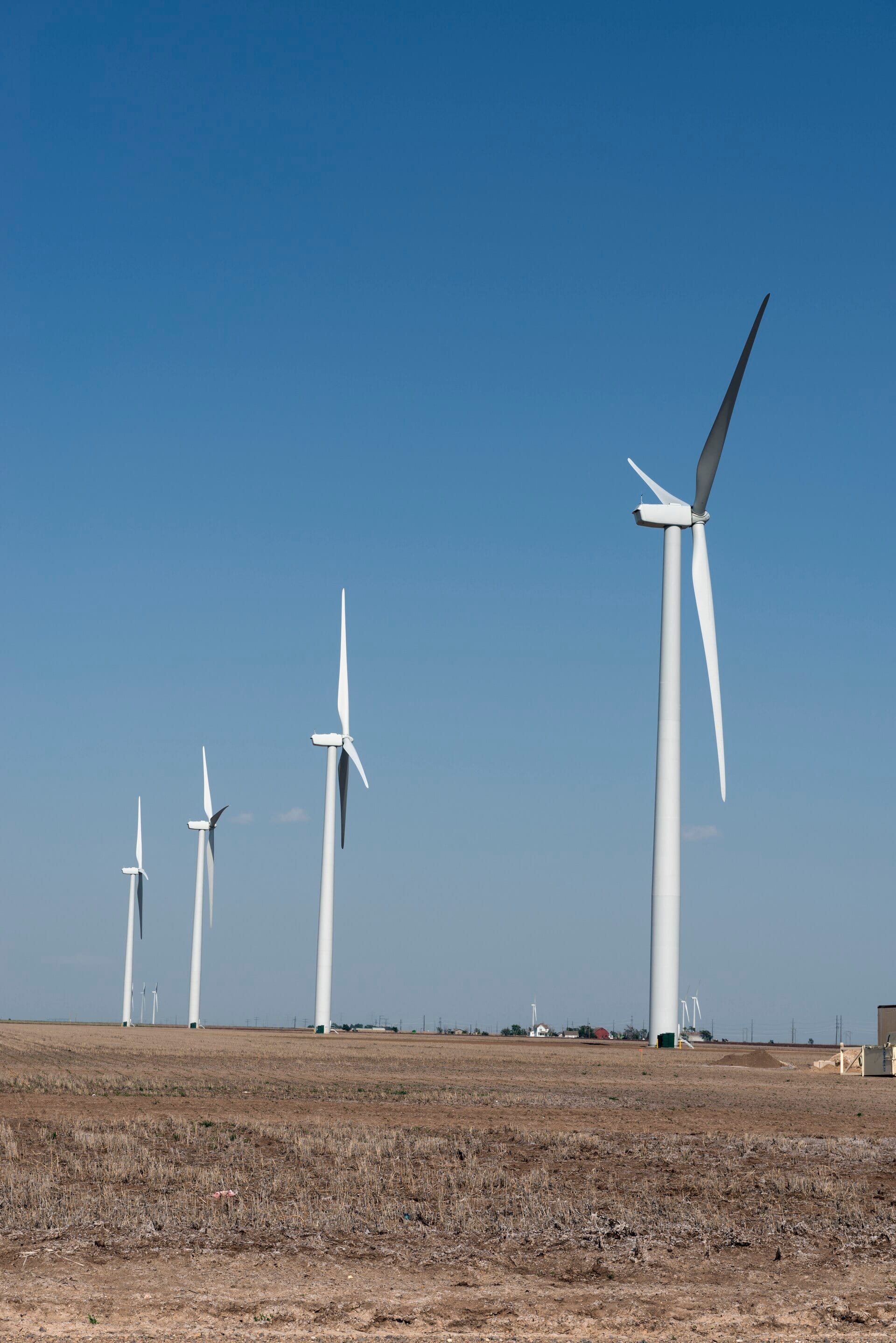 Tall white wind turbines in a dry farm field under a blue sky in the Texas Panhandle
