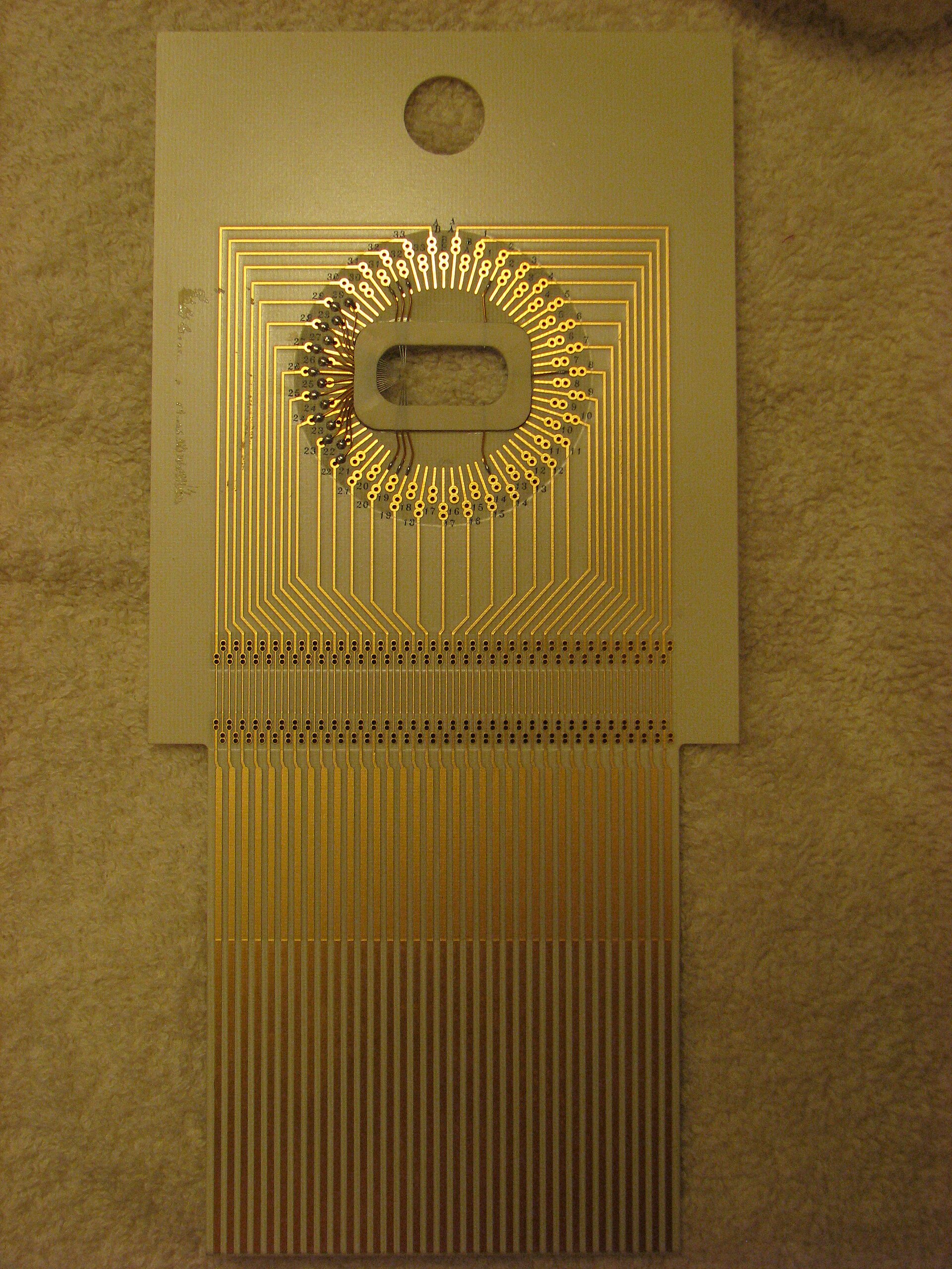Carte à pointes (wafer probe card) aux pistes dorées en contact avec une puce semi-conductrice