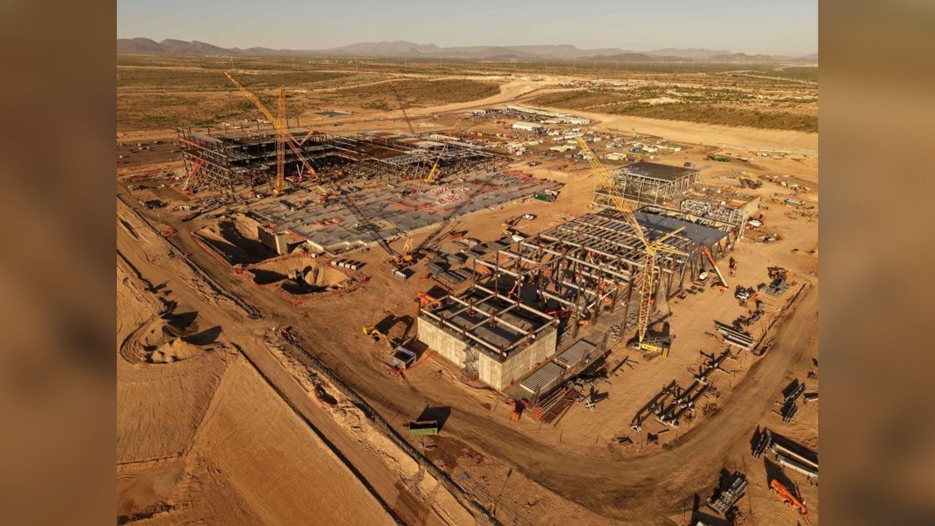 Aerial view of Amkor's Arizona advanced packaging campus under construction, cranes and steel frames rising out of the desert