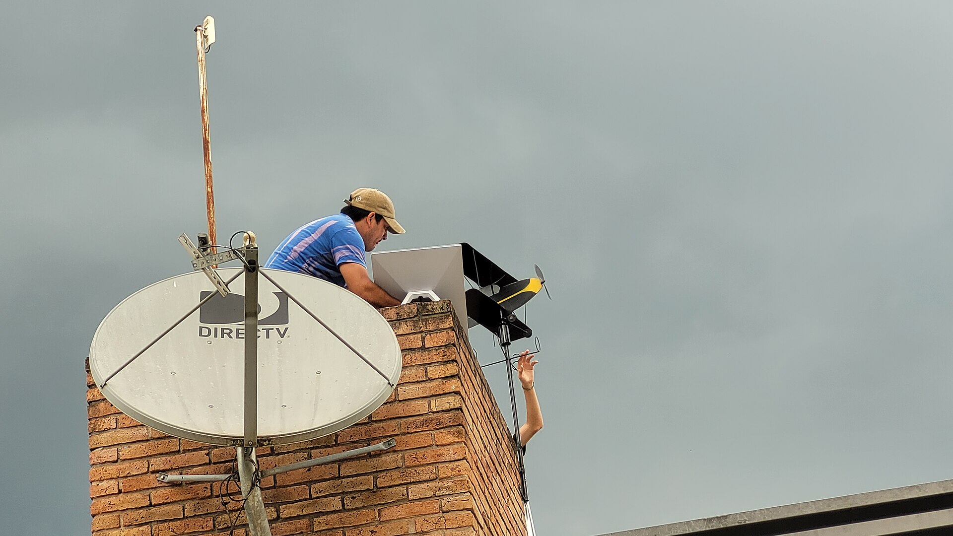 A technician installs a Starlink user terminal on a rooftop beside a satellite dish