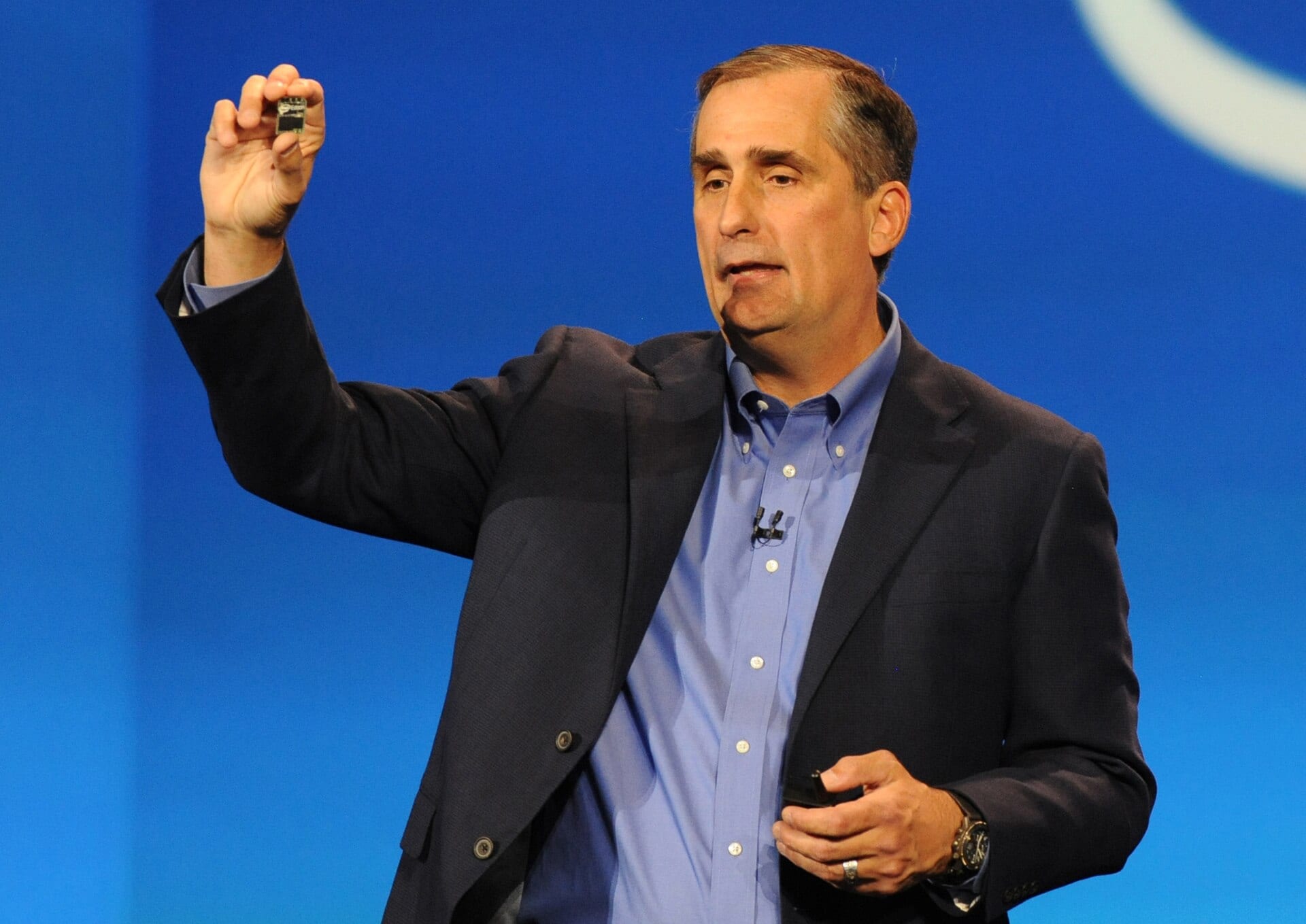 Brian Krzanich holds up a tiny Intel Edison chip module while speaking at a January 2014 launch event against a blue backdrop.