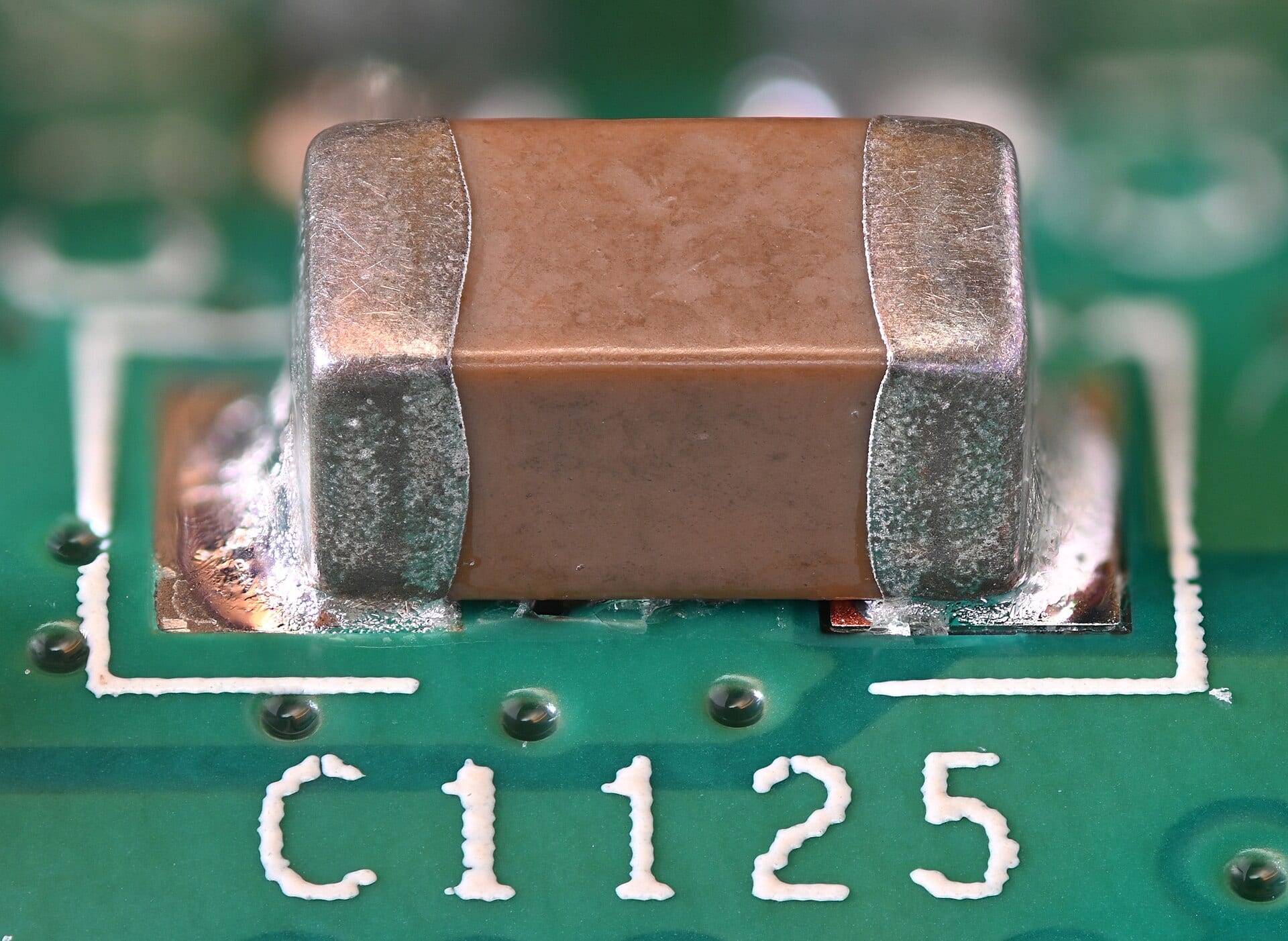 A multilayer ceramic capacitor soldered onto a green printed circuit board, seen in close-up