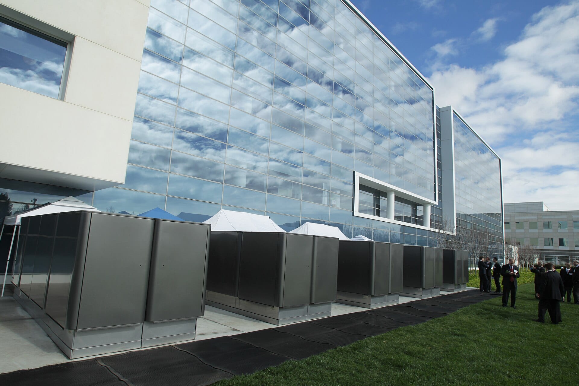 A row of Bloom Energy fuel-cell servers installed on paving outside a glass office building